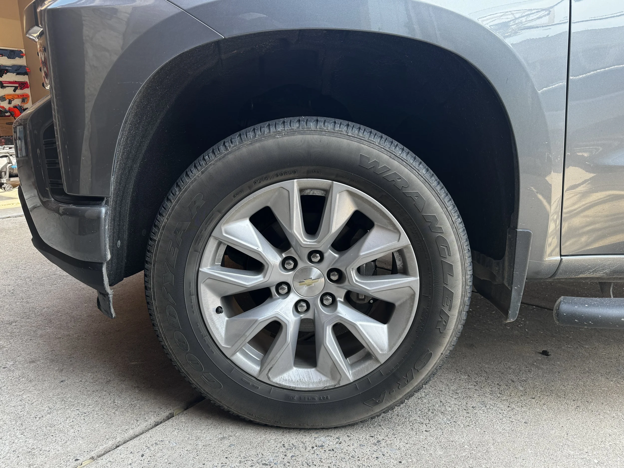 Close-up view of a vehicle's front wheel with a Chevrolet badge on the hubcap, fitted with Goodyear Wrangler tire, parked on a concrete surface.