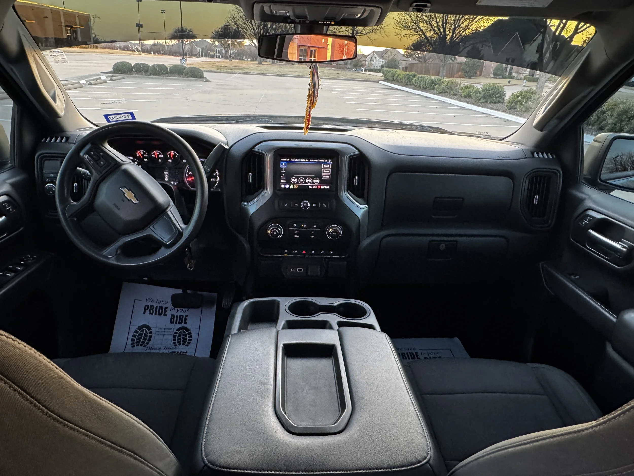Interior view of a Chevrolet pickup truck's dashboard and front seats, with a parking lot visible through the windshield.