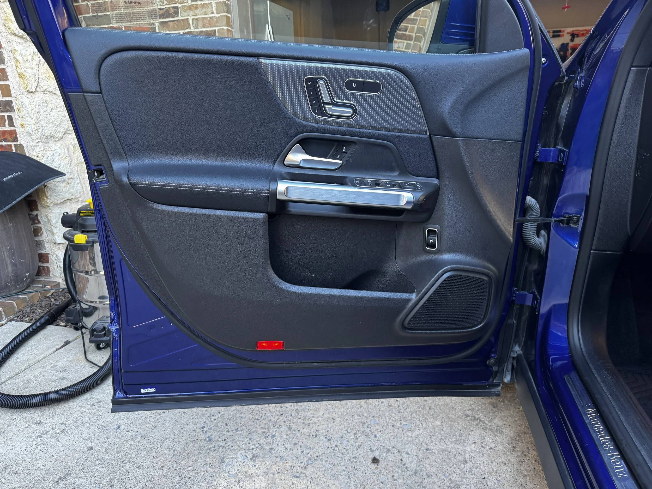 The interior driver-side door panel of a blue Mercedes-Benz vehicle featuring black material, silver door handle, and window control buttons.