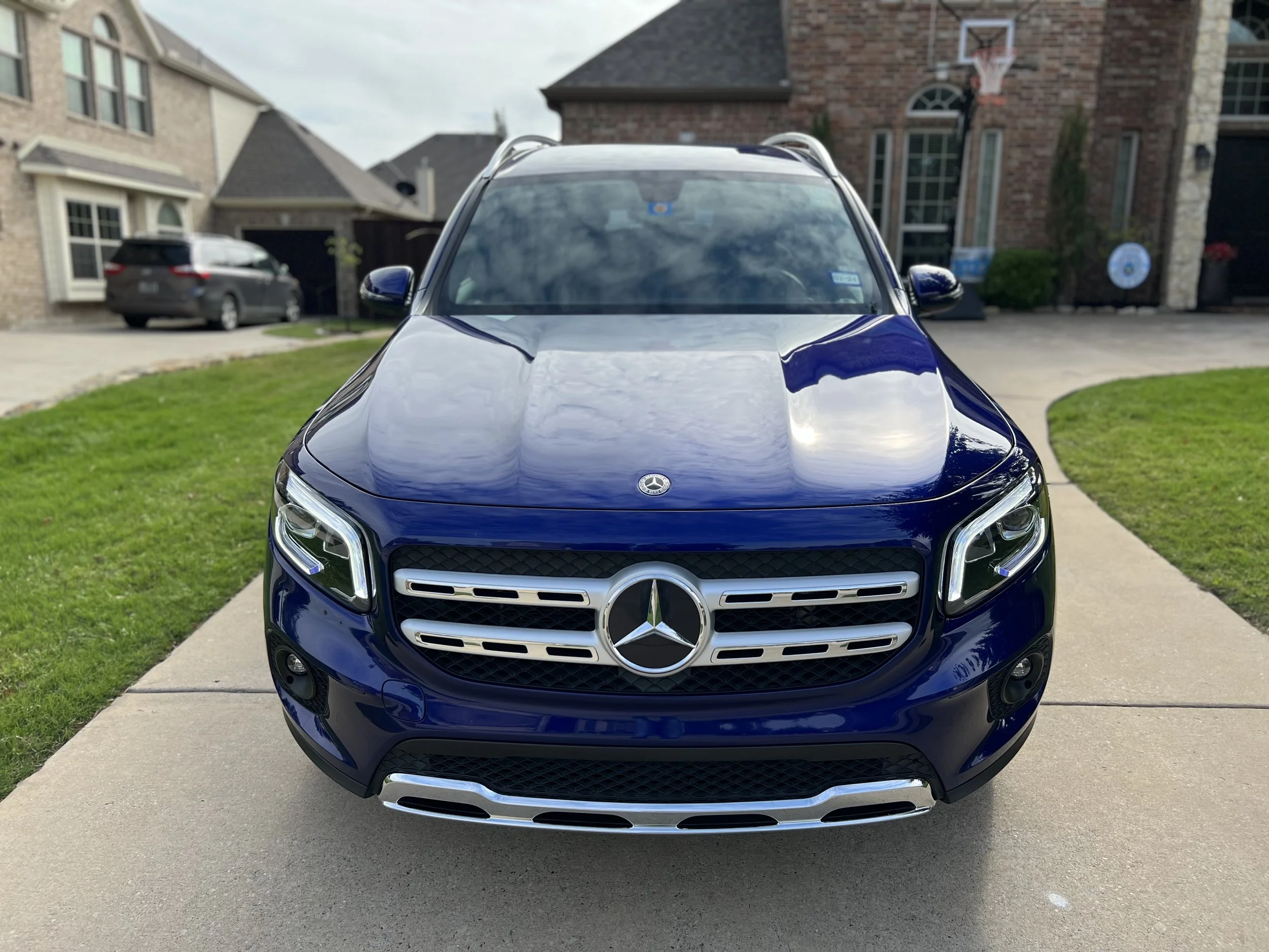Front view of a blue Mercedes-Benz SUV parked on a driveway with houses and other cars in the background.