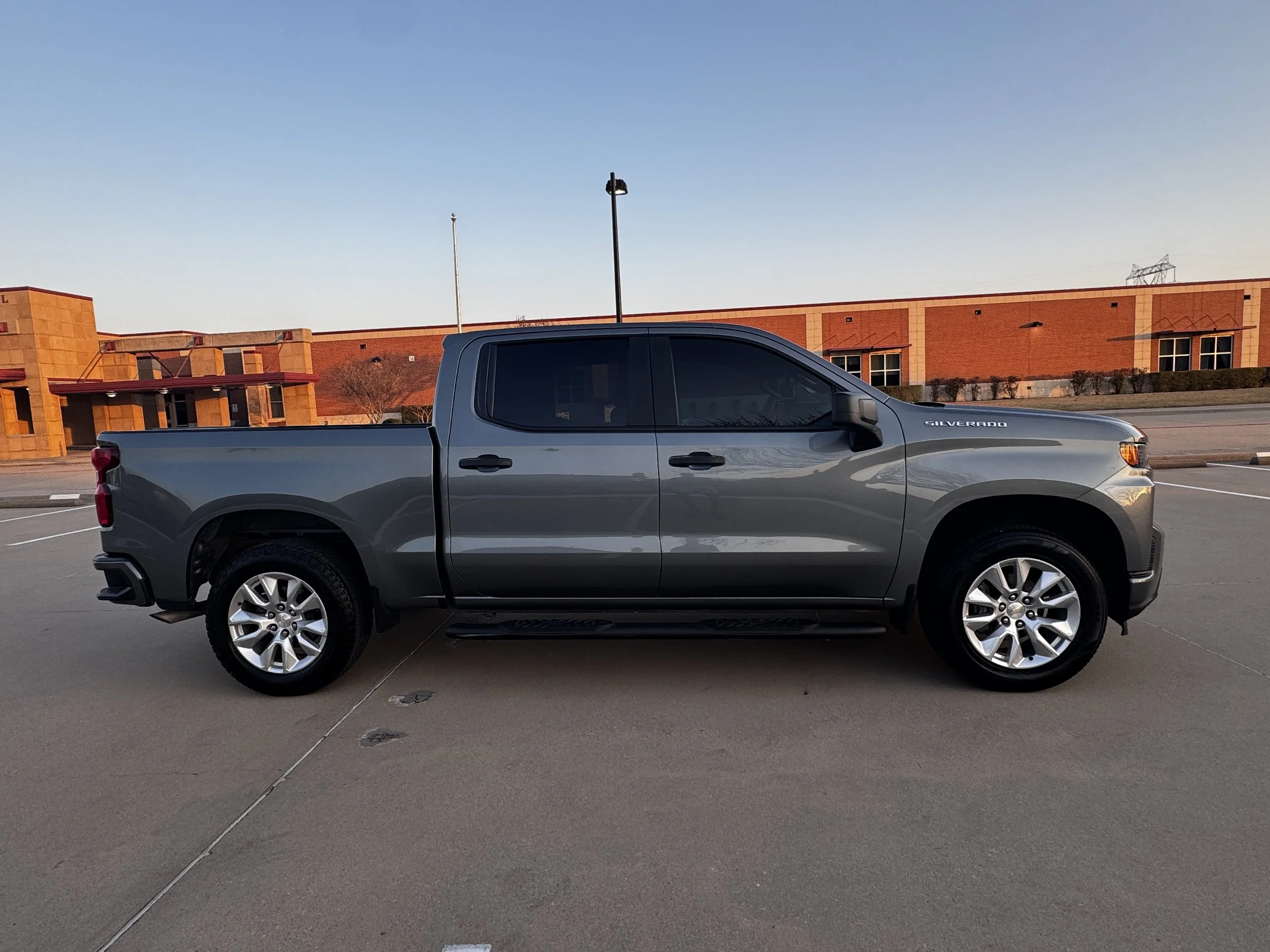 Side view of a gray Chevrolet Silverado pickup truck parked in an empty parking lot during sunset.