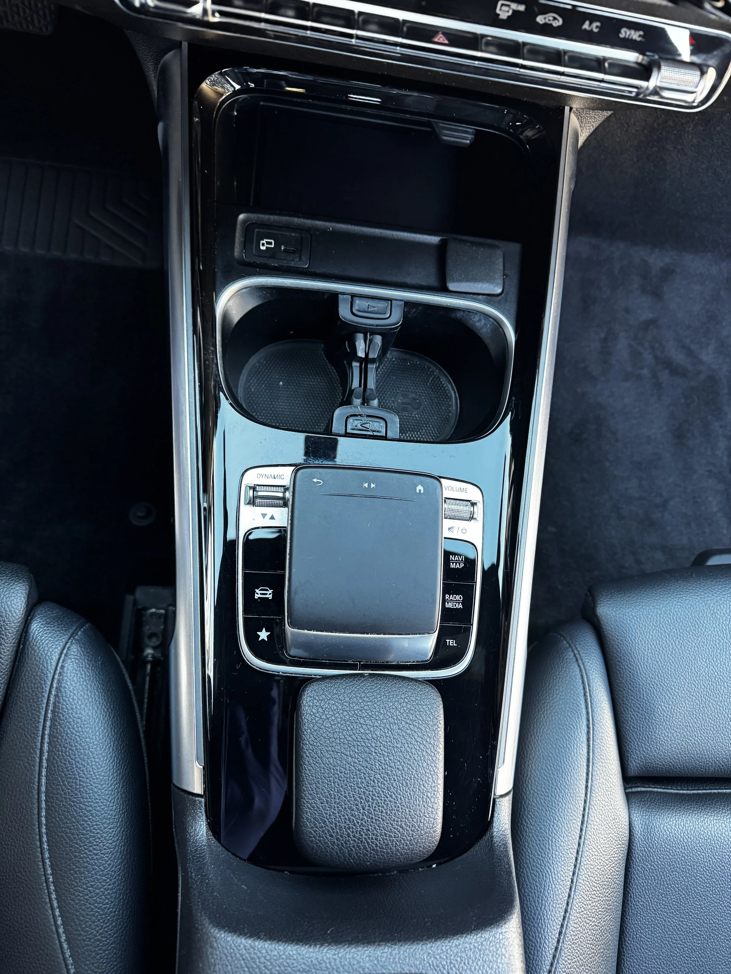 Center console of a car with a touch pad, cup holders, and various control buttons.