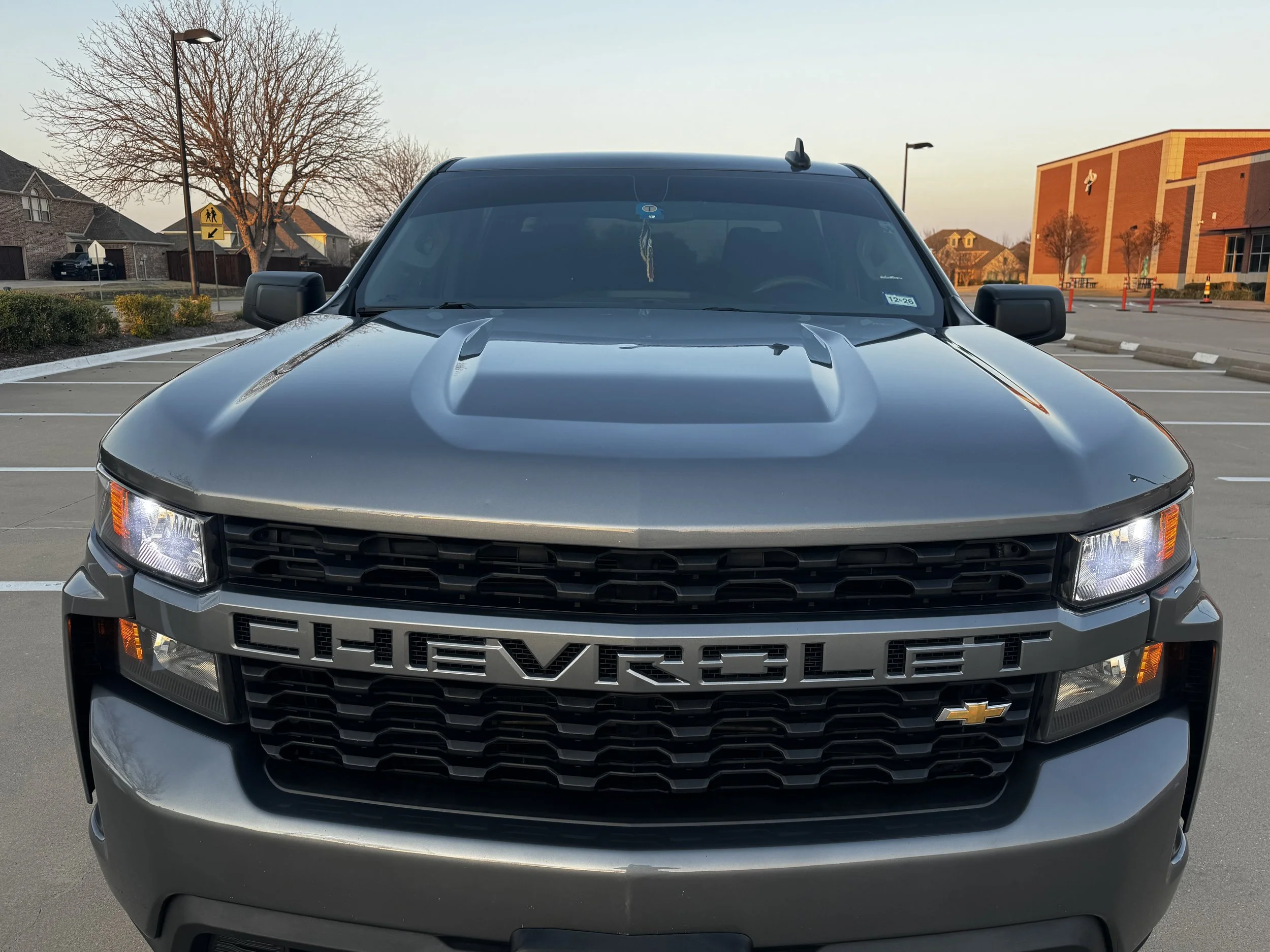 Front view of a gray Chevrolet pickup truck parked in an empty parking lot during sunset.