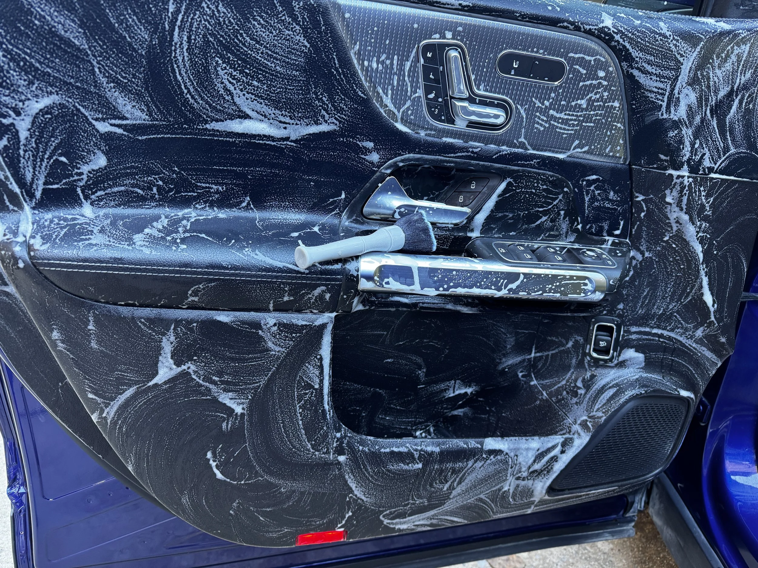 Car door interior covered in soap and foam, with a white handle, window controls, and seat adjustment controls visible.