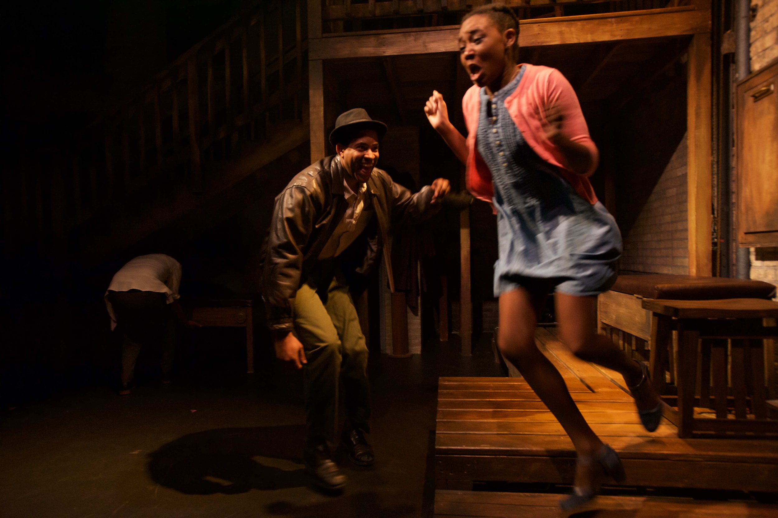 Theatre performance still of Ashli Rene Funches standing on a table during a dramatic stage scene with a fellow actor.
