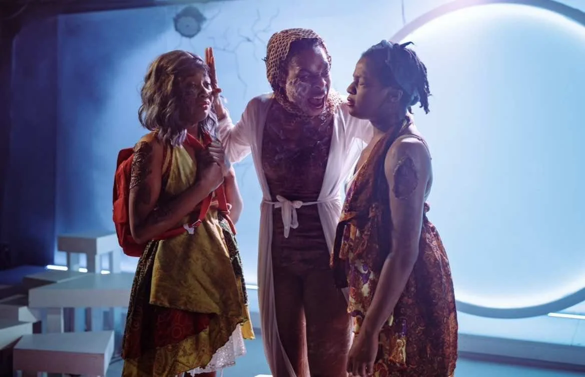 Performance still of Ashli Rene Funches (left) in the stage production "Is God Is" with Karen Aldridge under blue stage lighting.