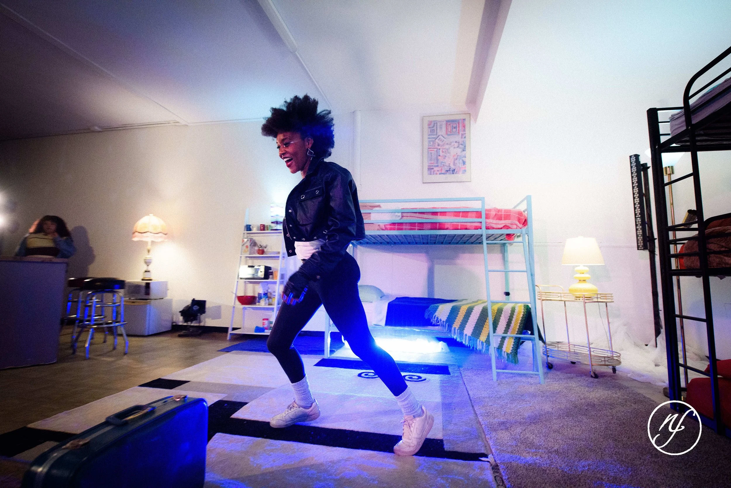 Theatre performance still of Ashli Rene Funches dancing in a loft-style set during a staged performance with another actor in the background.