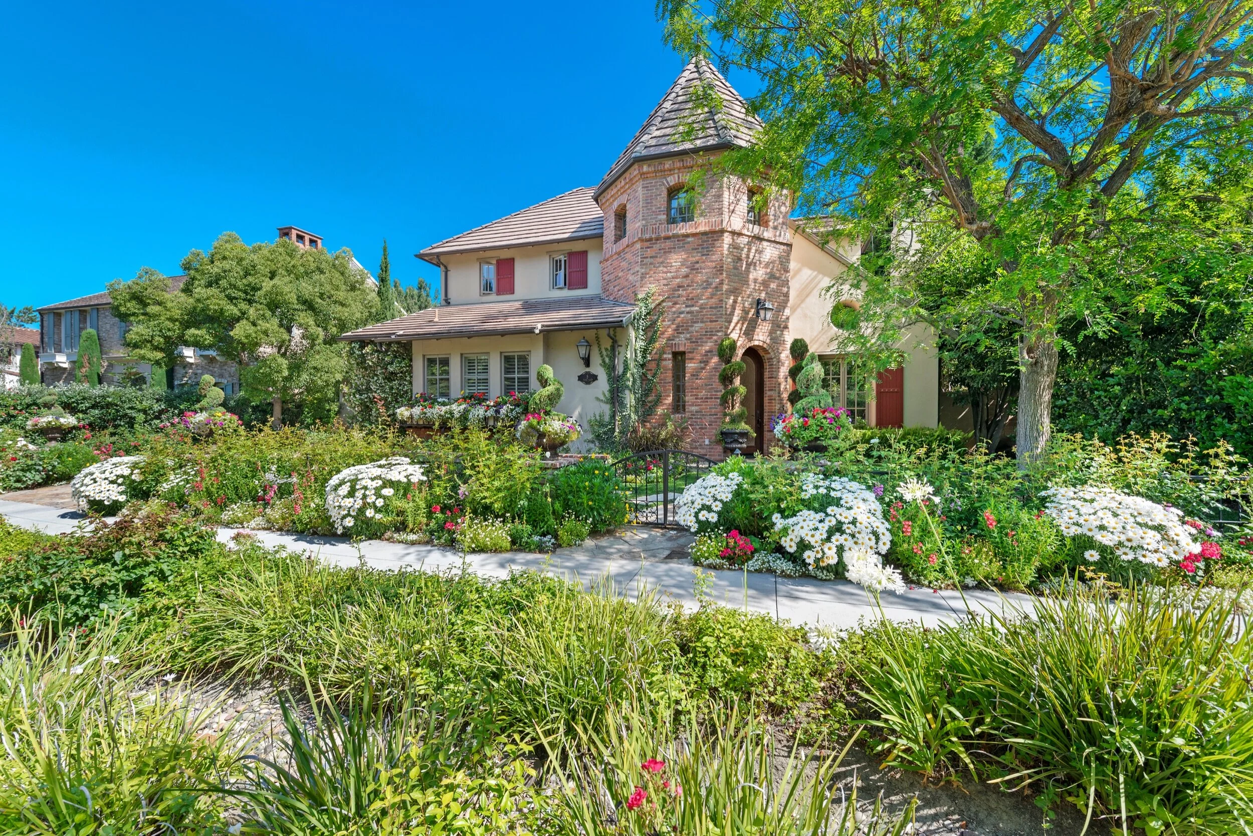 Colorful house with a lush garden full of blooming flowers and trees, sunny day with a bright blue sky.