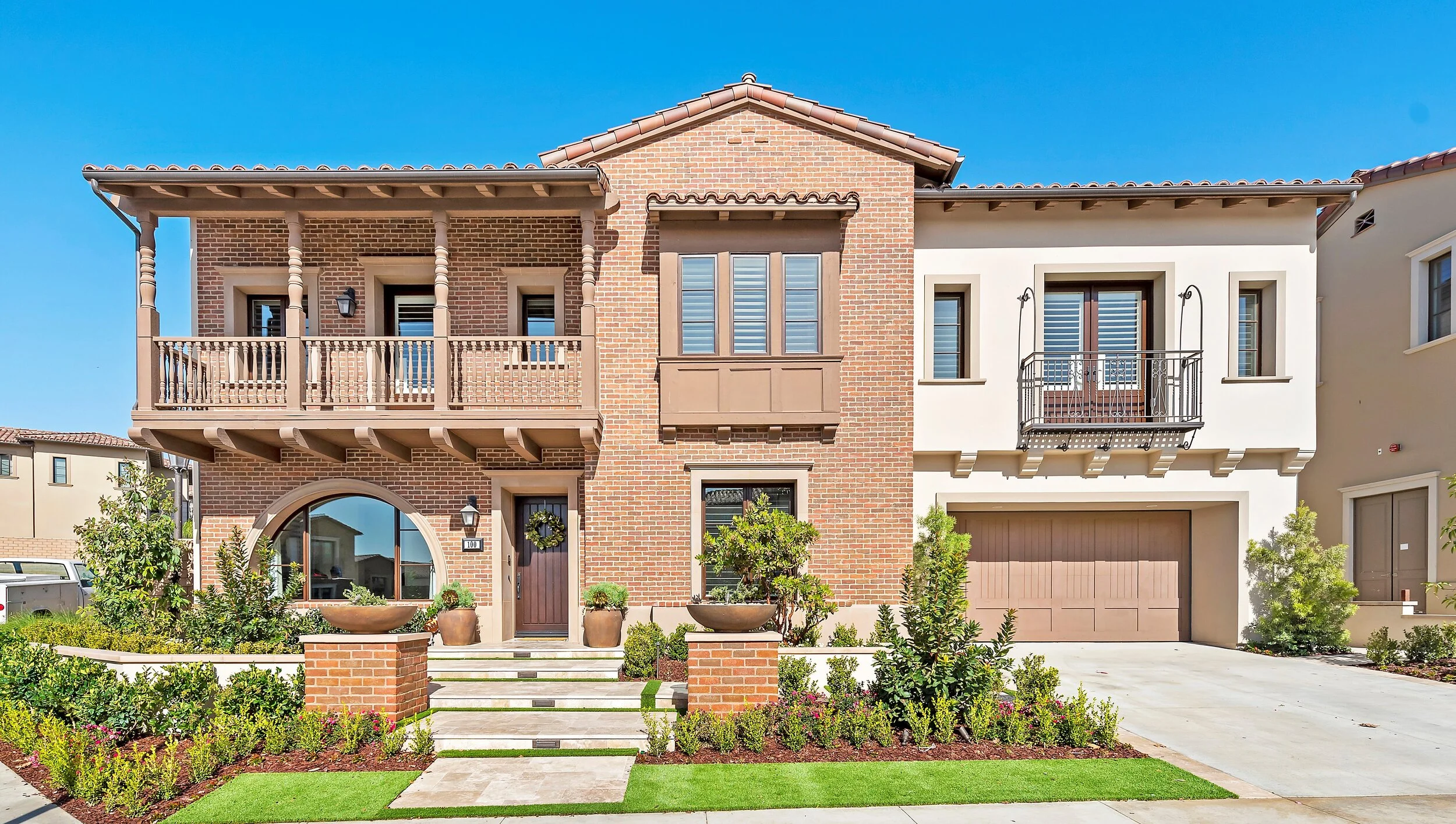Modern house with brick and white exterior, two balconies, and well-maintained front yard.