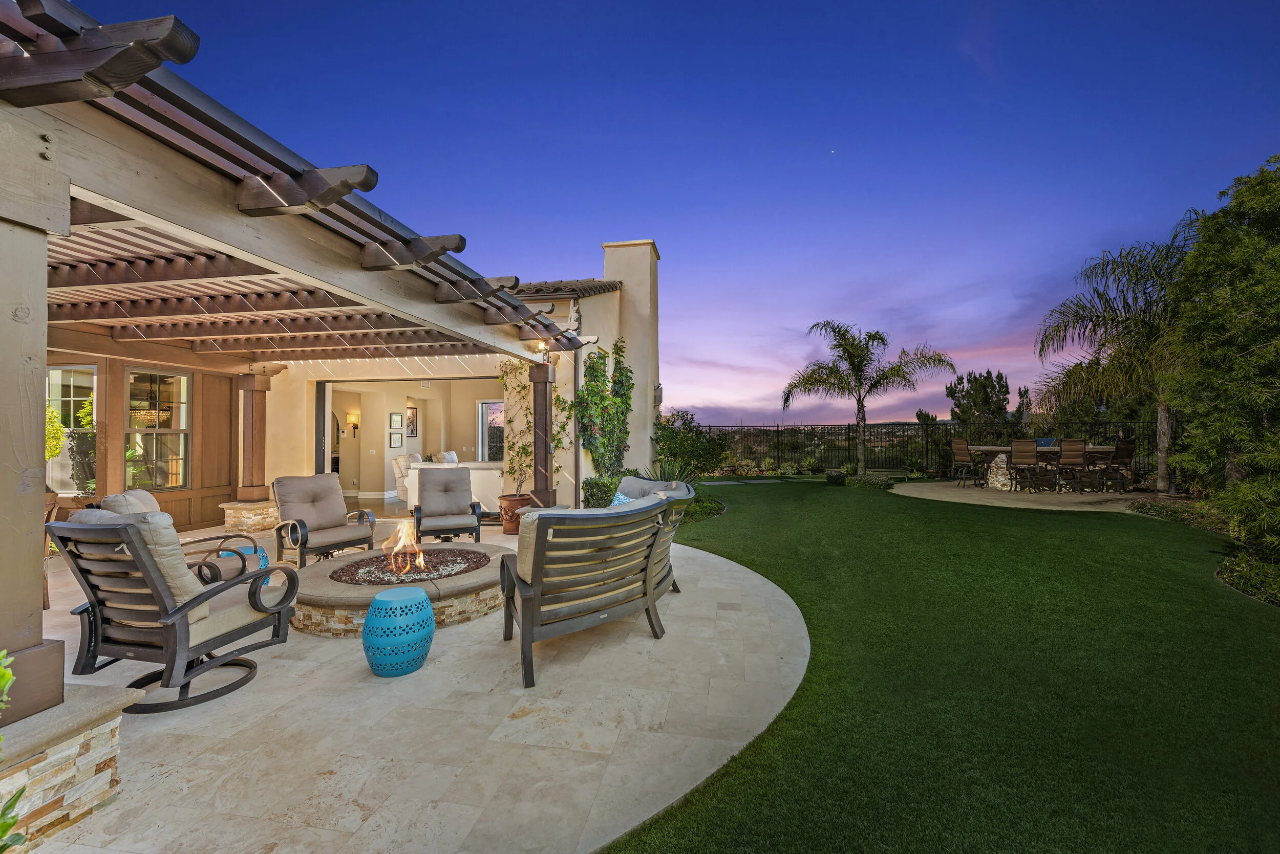 Outdoor patio with seating area, fire pit, and lush green lawn at sunset.