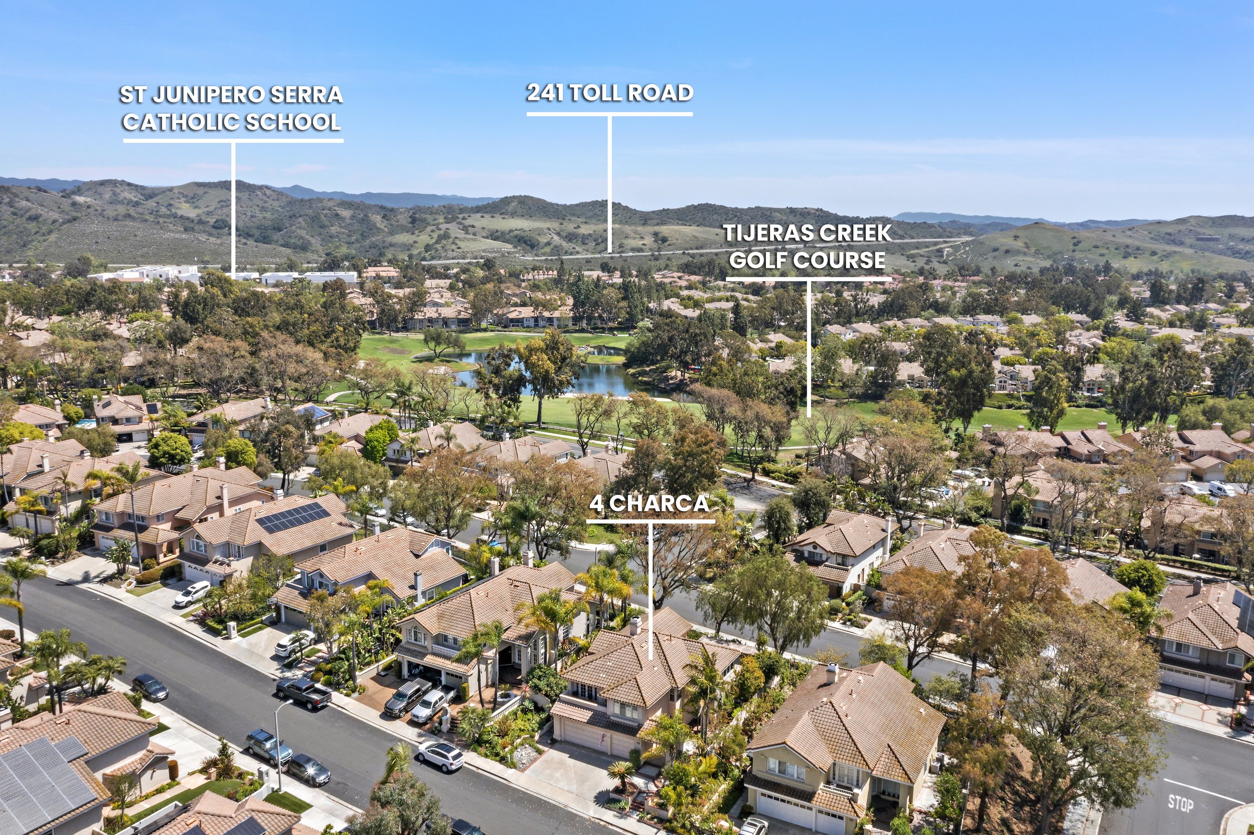 Aerial view of a residential neighborhood with houses, trees, a golf course, a creek, and hills in the background, with labels indicating St. Junipero Serra Catholic School, 241 Toll Road, Tijerass Creek Golf Course, and 4 Charca.