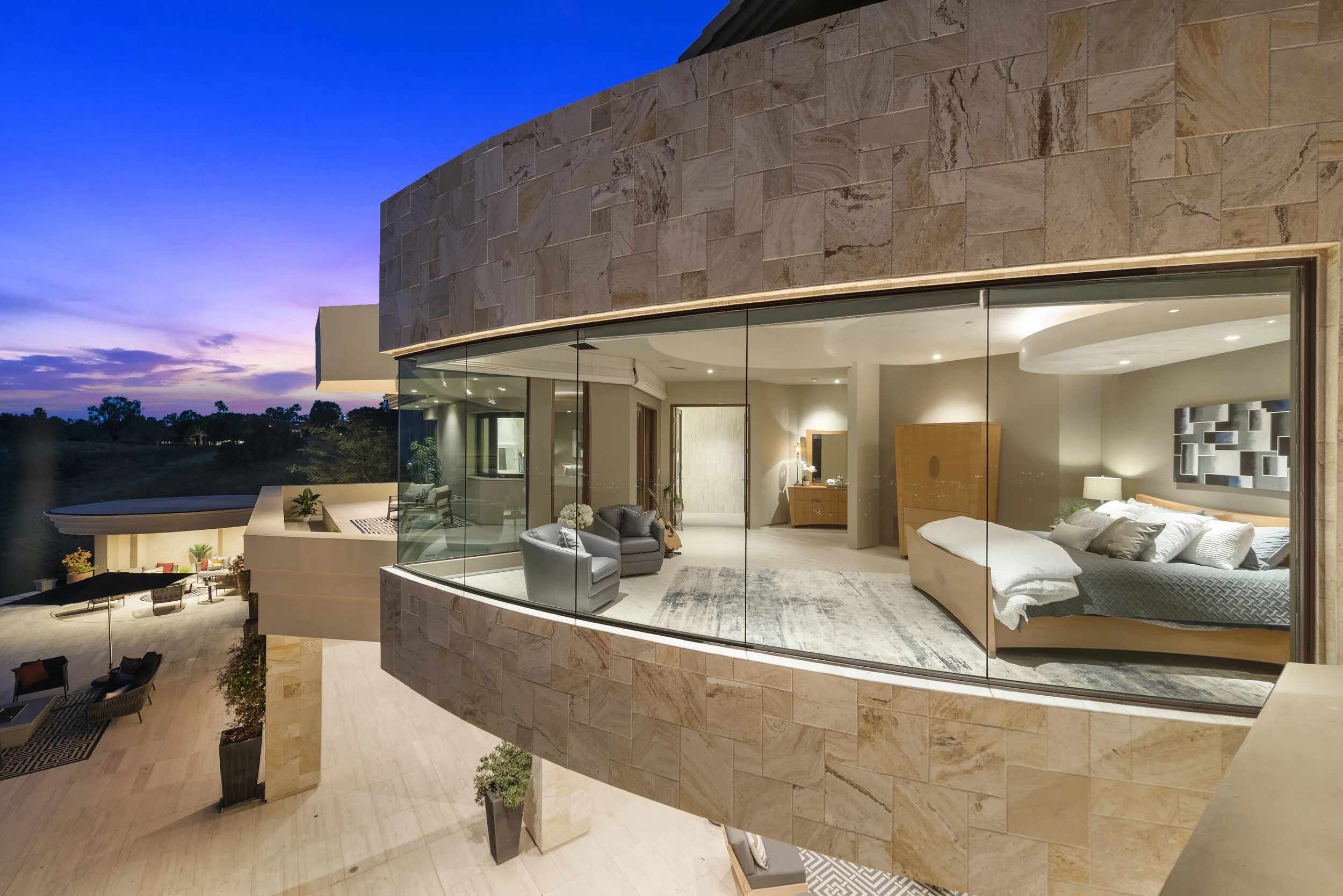 Luxury modern bedroom with large glass windows, contemporary furniture, and scenic sunset view.