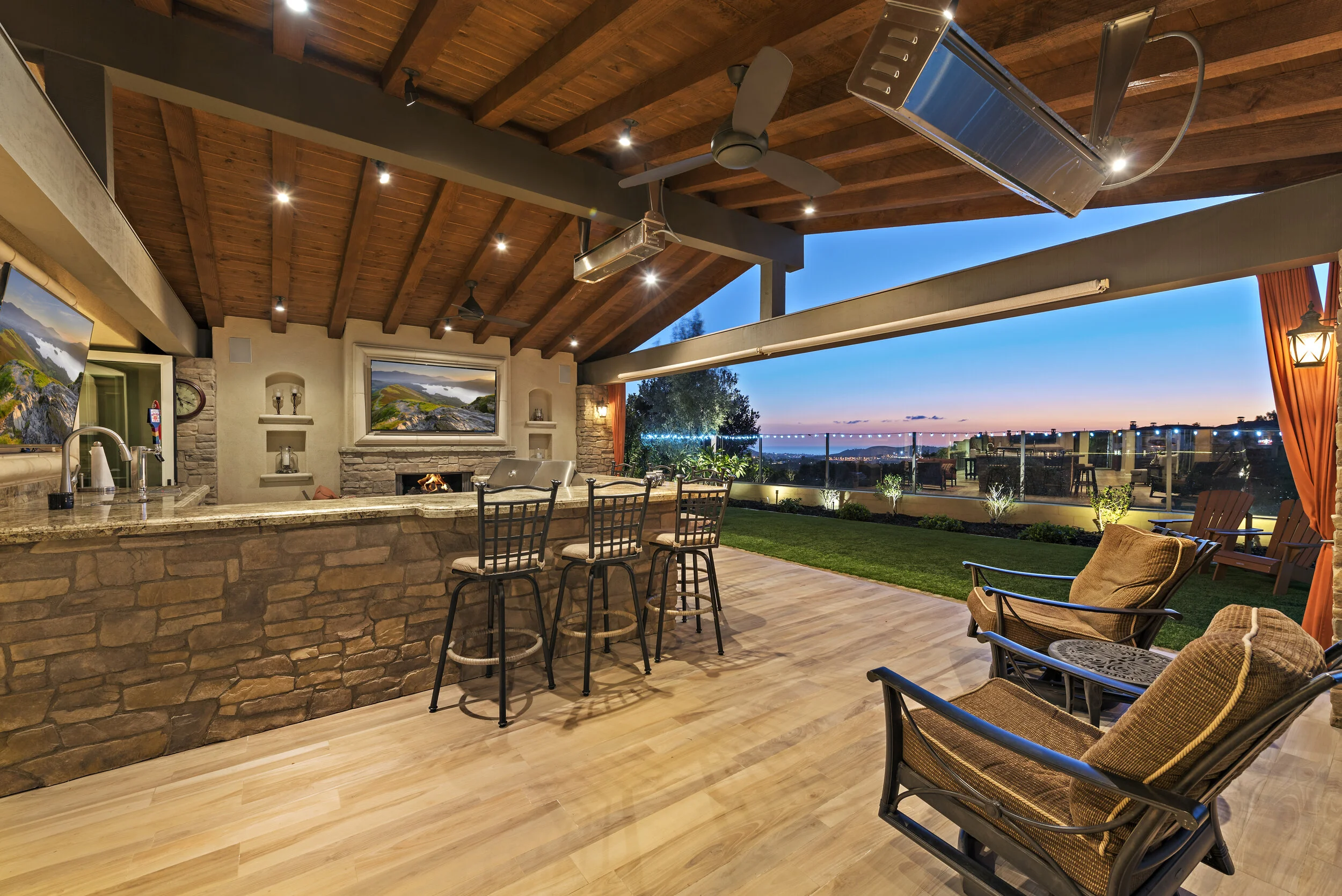 A spacious outdoor patio with a bar area, comfortable seating, and a view of a city skyline at sunset
