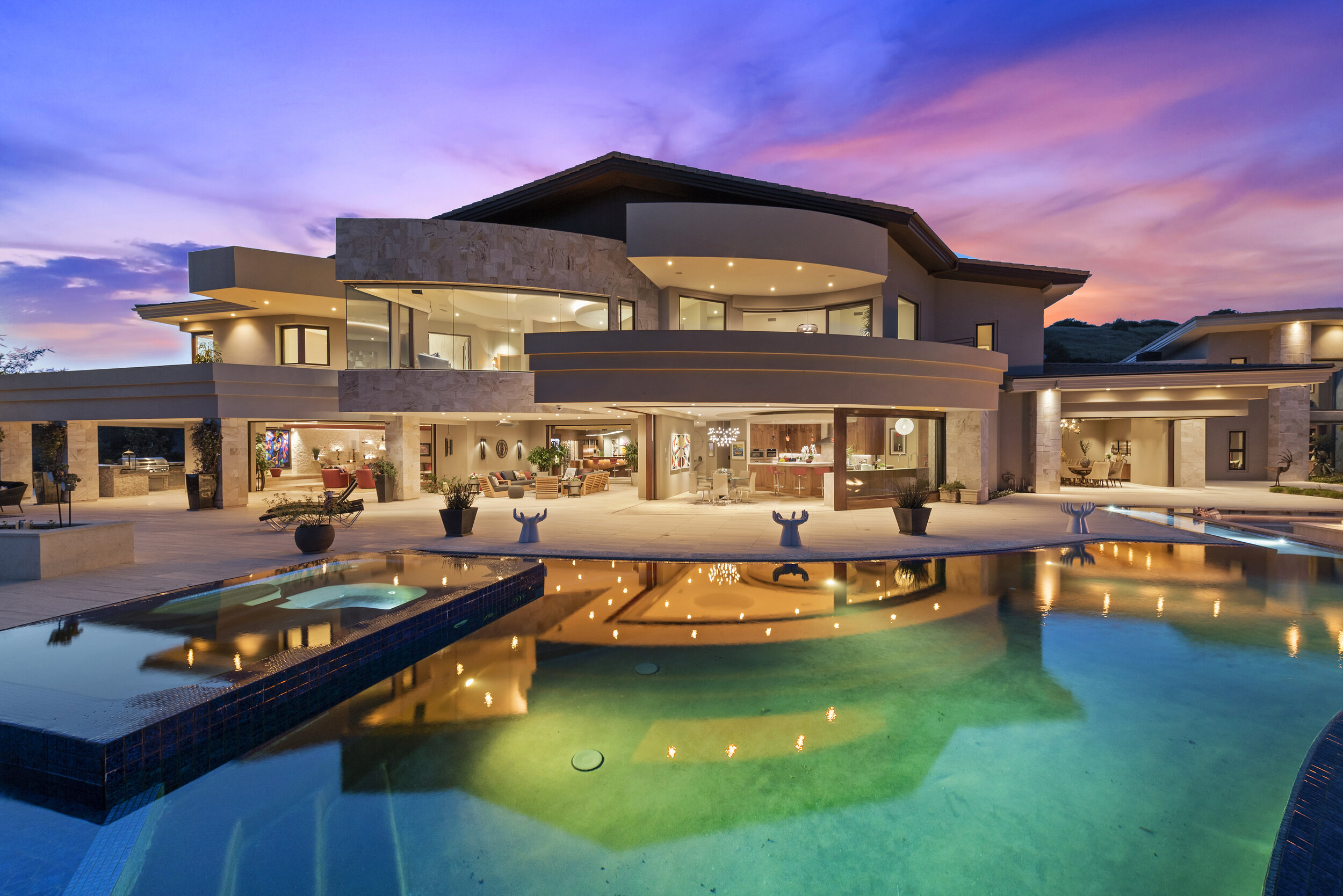 Luxury modern house with large glass windows, outdoor patio, swimming pool, and sunset sky
