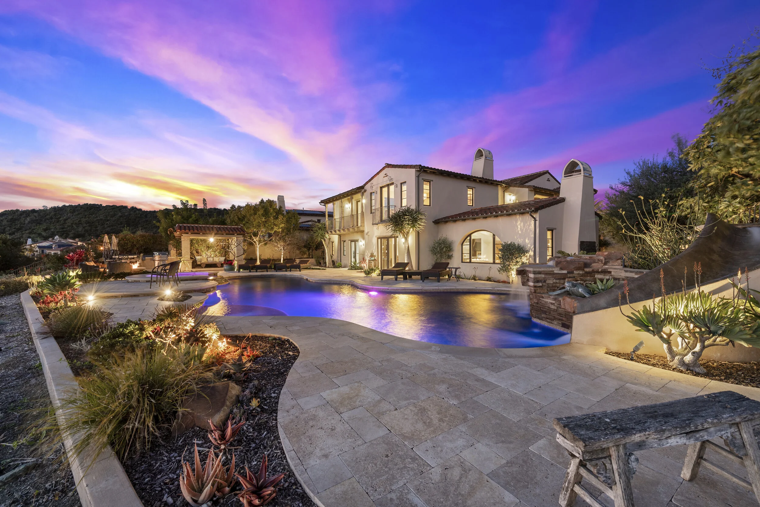 Luxury backyard with a swimming pool, outdoor seating, and a two-story house during sunset