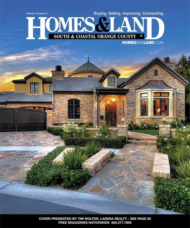Cover of Home & Land magazine showing a large, elegant house with stone and brick exterior, landscaped front yard with stone pathway, and sunset sky background.