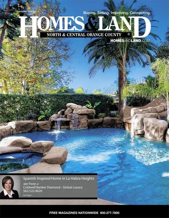 Cover of Homes & Land magazine featuring a backyard with a swimming pool, large rocks, and palm trees against a clear blue sky.