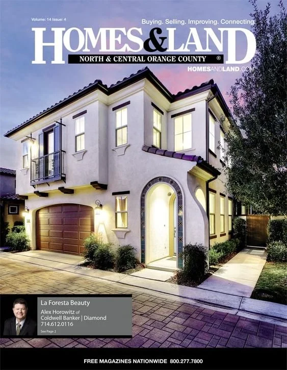 Front view of a two-story house with a garage, illuminated at dusk, on the cover of Homes & Land magazine.