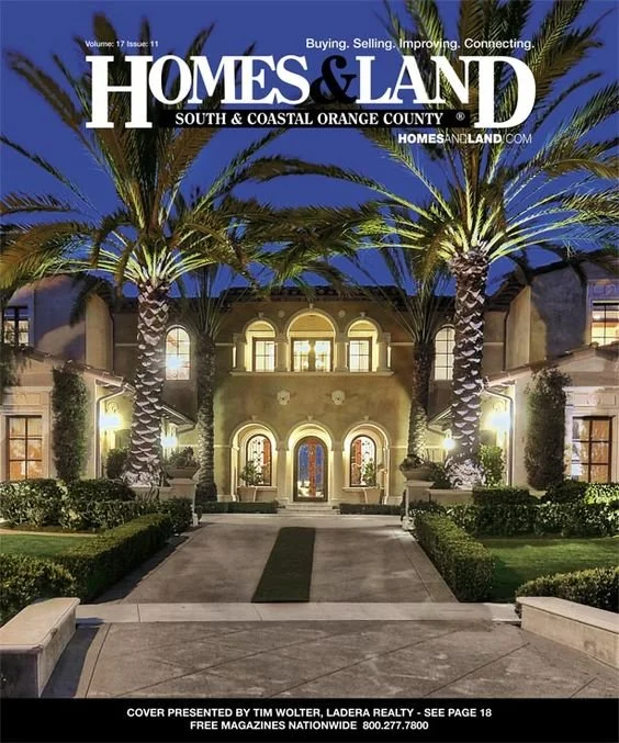 Nighttime view of a large luxurious house with palm trees in front, illuminated exterior lighting, well-maintained bushes, a paved walkway, and glowing windows. The house has an elegant, Mediterranean-style architecture.