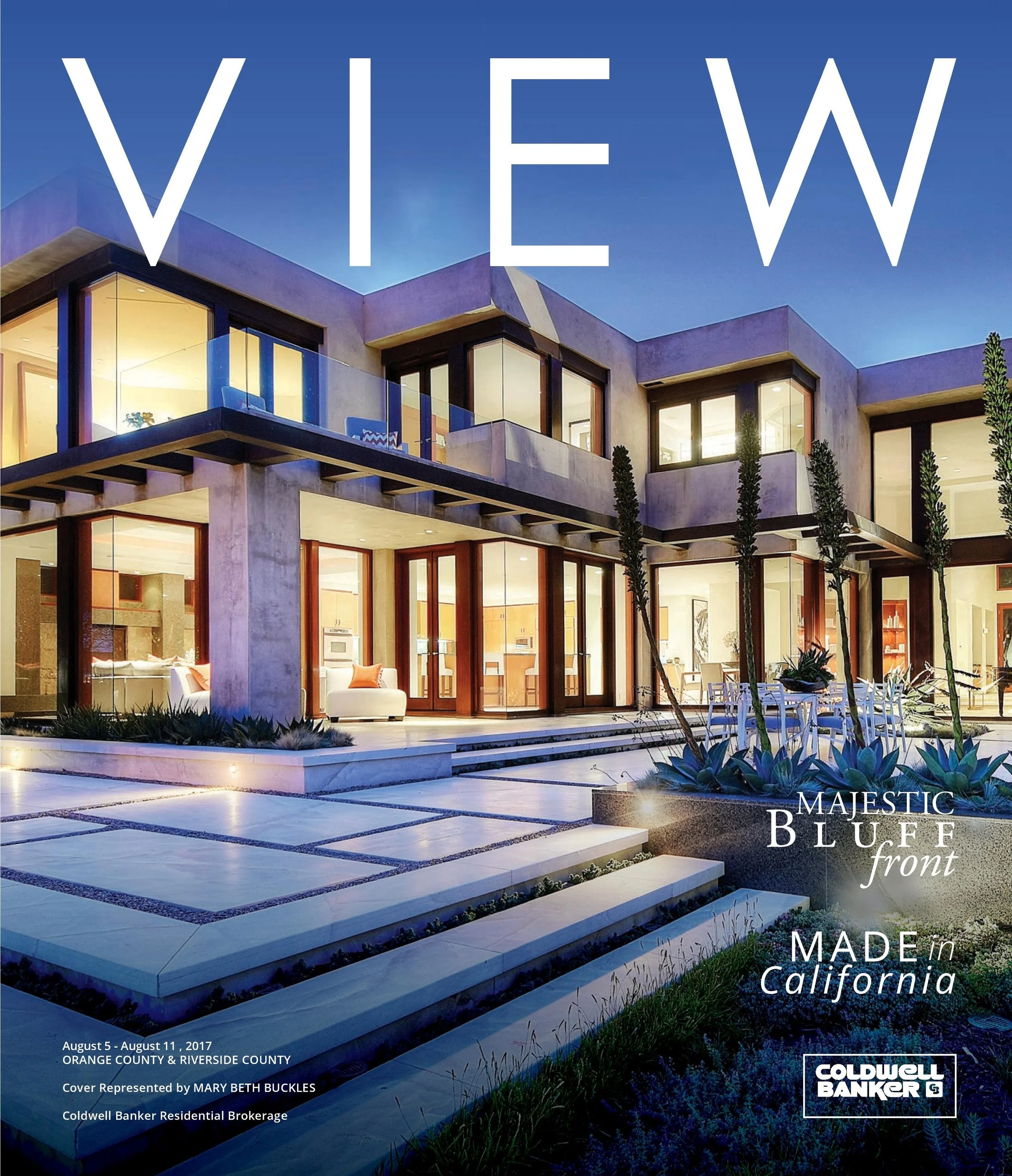 Modern luxury house with large glass windows, outdoor patio, and landscaped yard at dusk, featured on a real estate magazine cover.