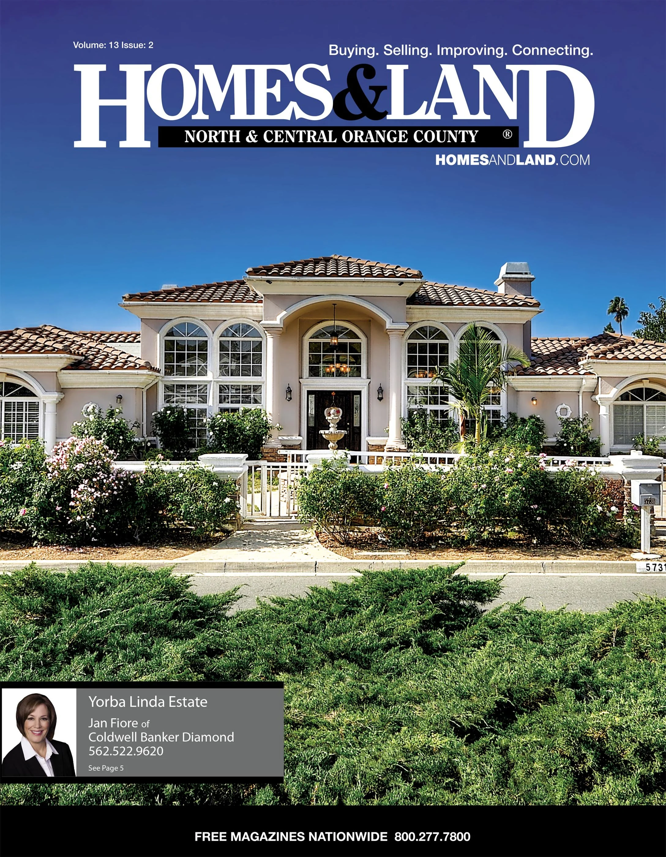 Cover of Homes & Land magazine featuring a large, elegant house with a tiled roof, large arched windows, and surrounded by lush shrubbery, under a bright blue sky.