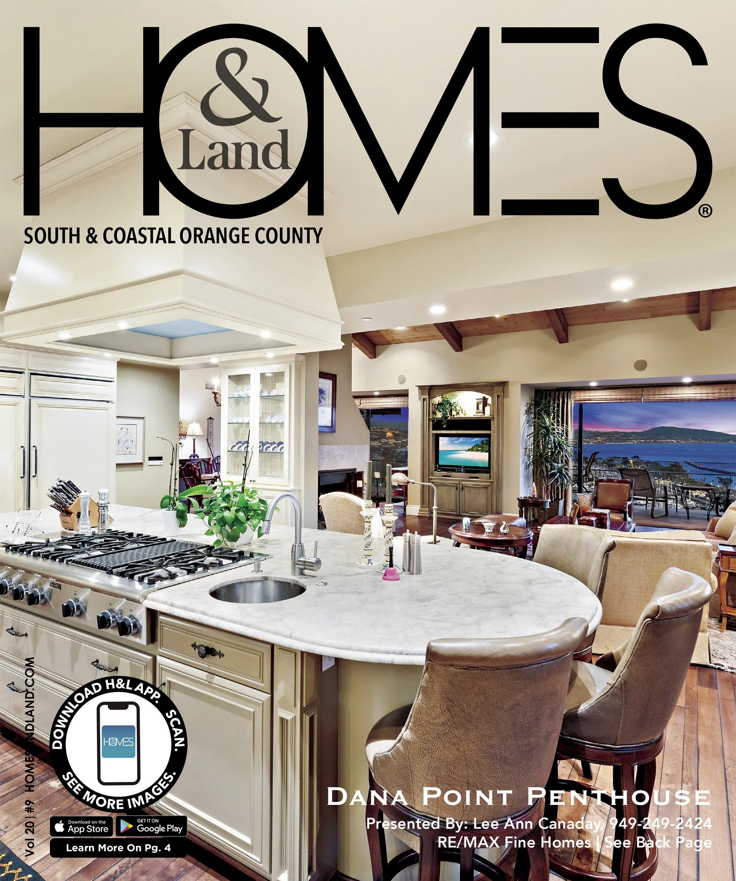 Interior view of a luxurious kitchen and living room area with large windows overlooking water and mountains; the kitchen features a white island with a sink, stove, and bar stools.