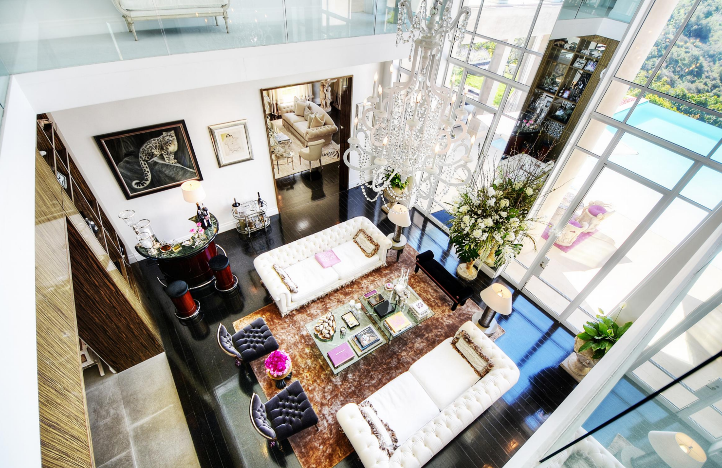 A luxurious living room with large glass windows, white sofas, a chandelier, a large floral arrangement, and various decorative items.