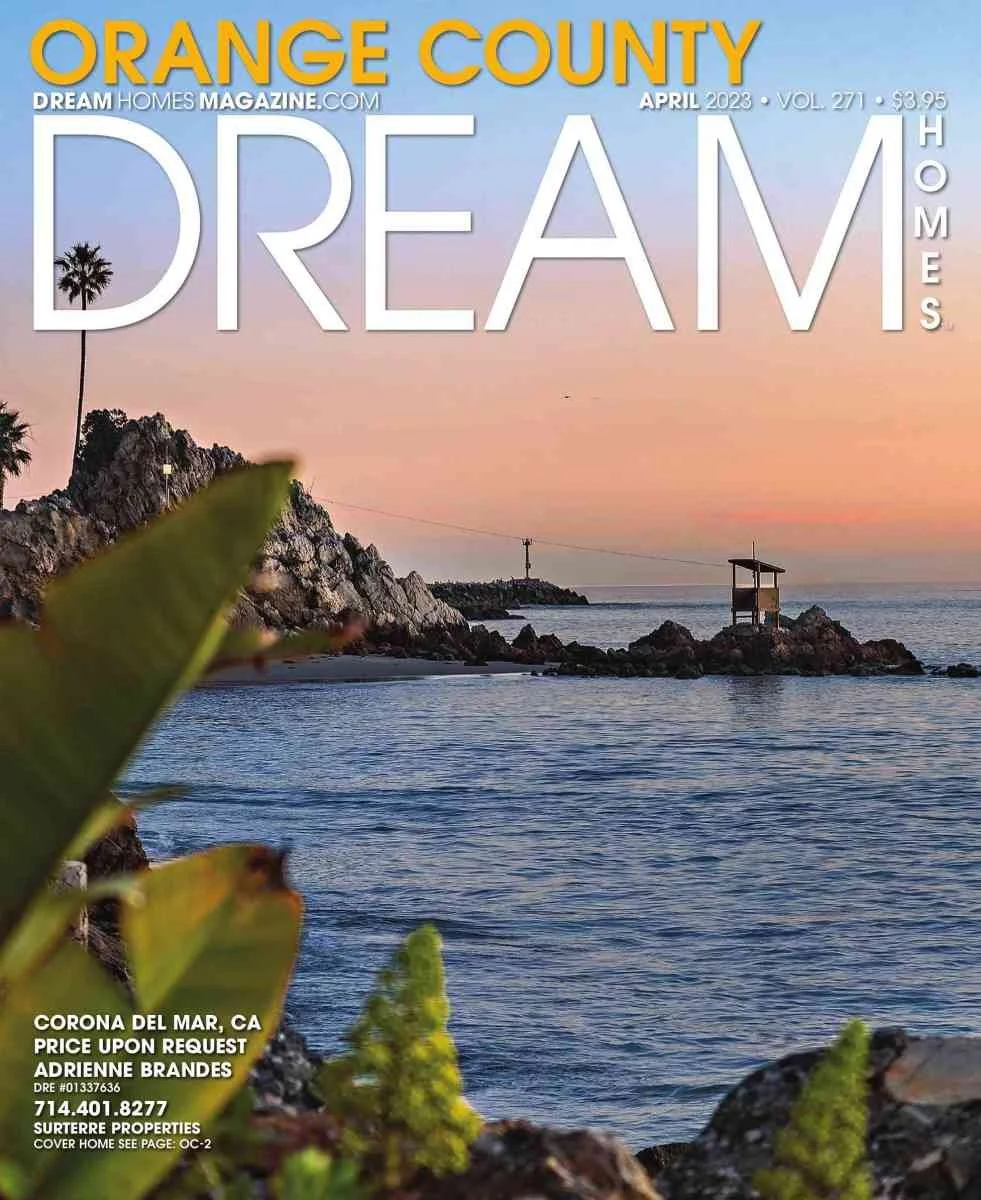 Magazine cover for Orange County Dream Homes from April 2023 featuring a coastal sunset scene with rocks, water, a small structure on rocks, and a palm tree on a hill.