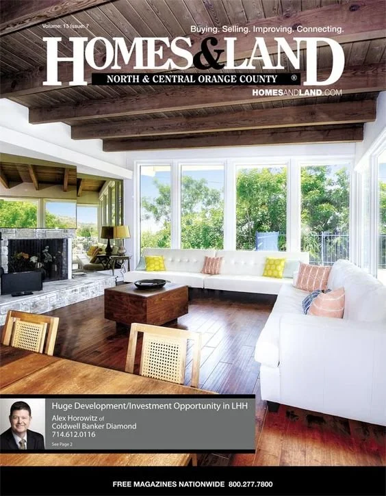 Living room with large windows, white sectional sofa, wooden coffee table, and hardwood floors, with a view of green trees outside.