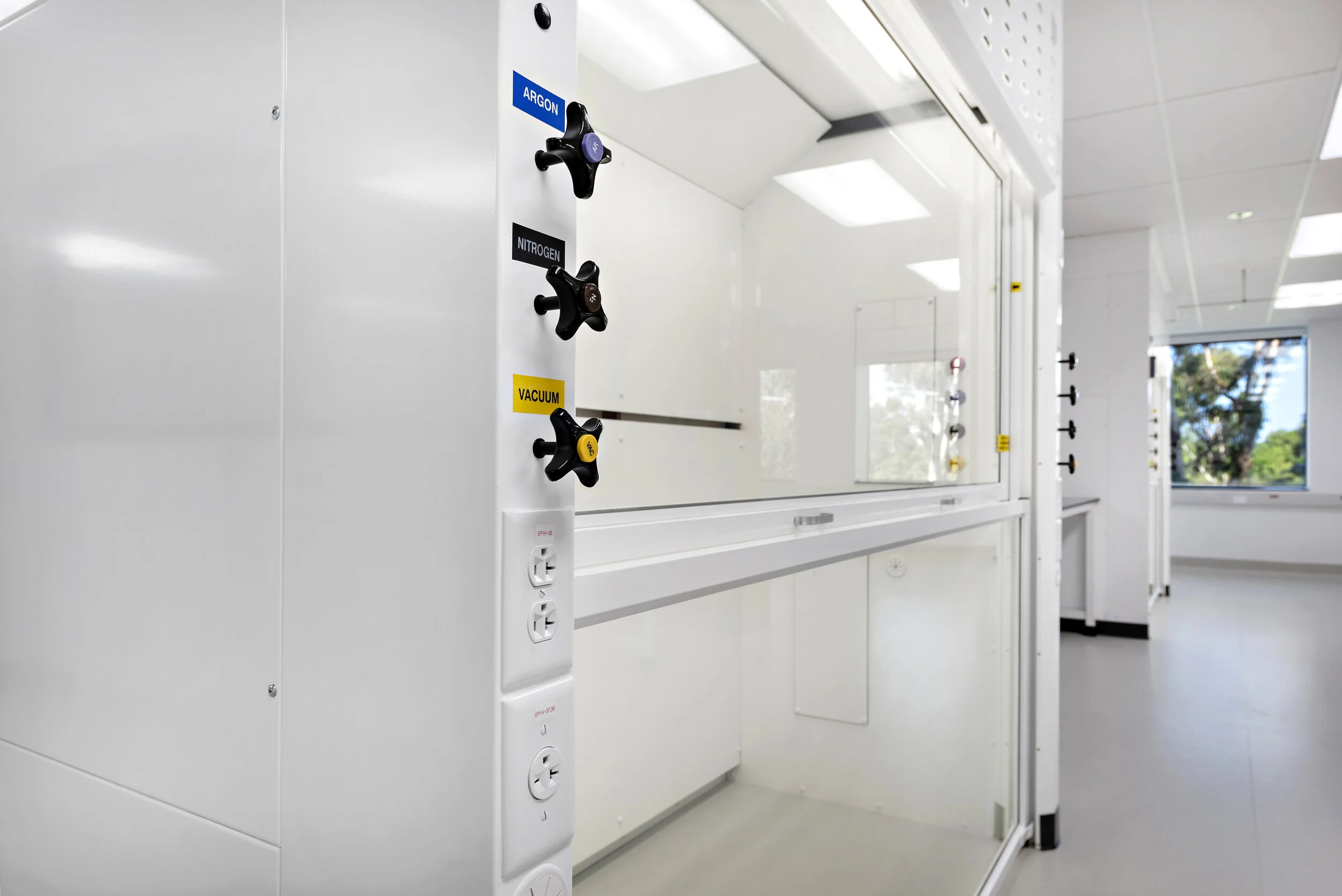 Supply cabinet with gas controls labeled Argon, Nitrogen, and Vacuum, located in a laboratory with window and white walls.