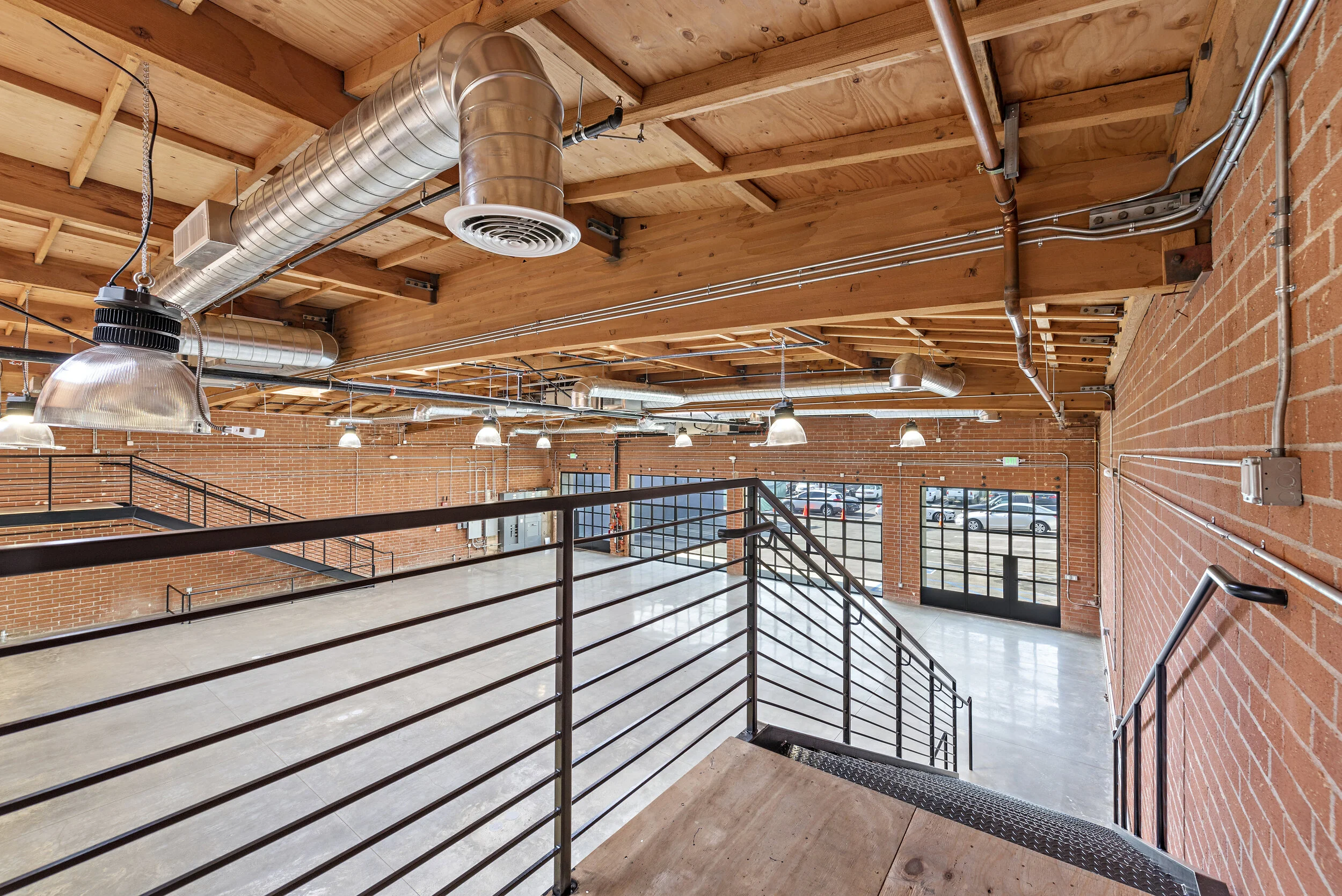 Interior of a modern industrial-style building with exposed brick walls, a wooden ceiling with visible beams, metal ductwork, and large windows.