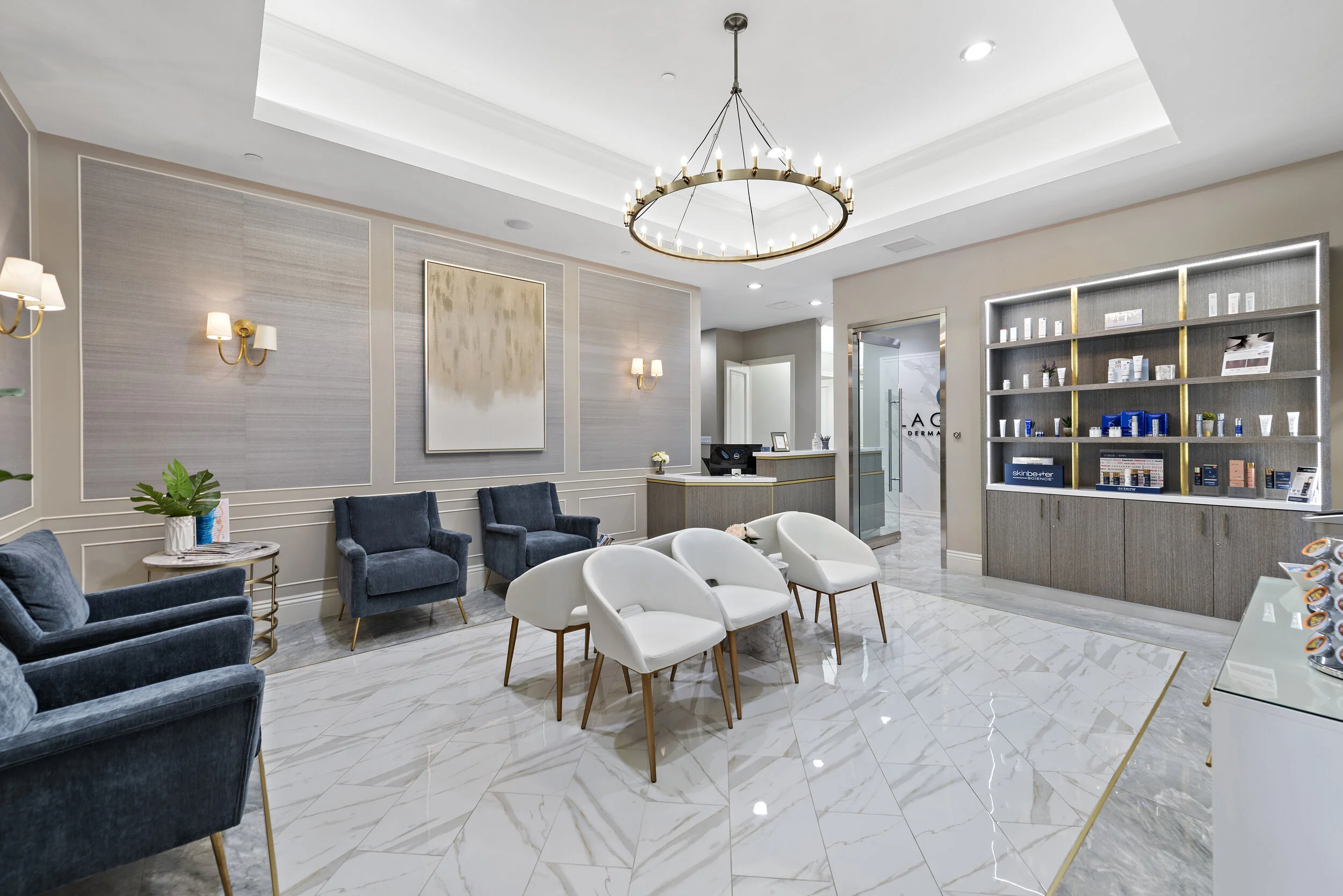 Clean and modern medical or beauty clinic waiting room with white and blue chairs, marble flooring, wall art, built-in shelving with products, and a reception desk.