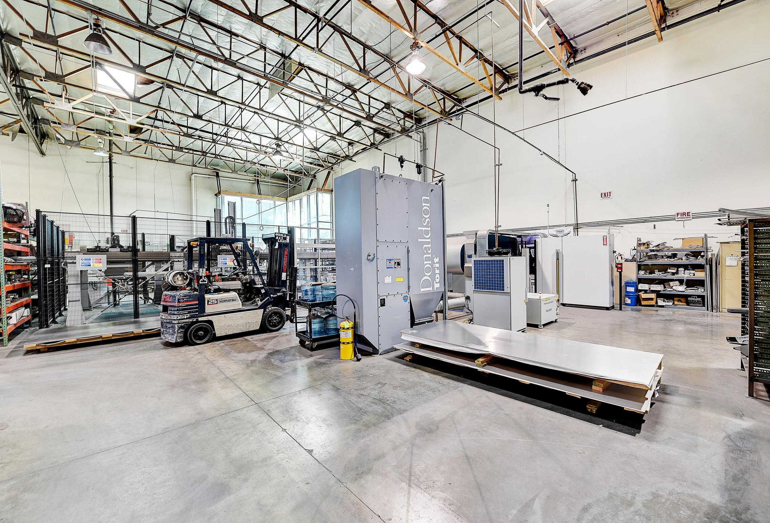 Empty industrial warehouse with machinery, shelving, and a forklift.