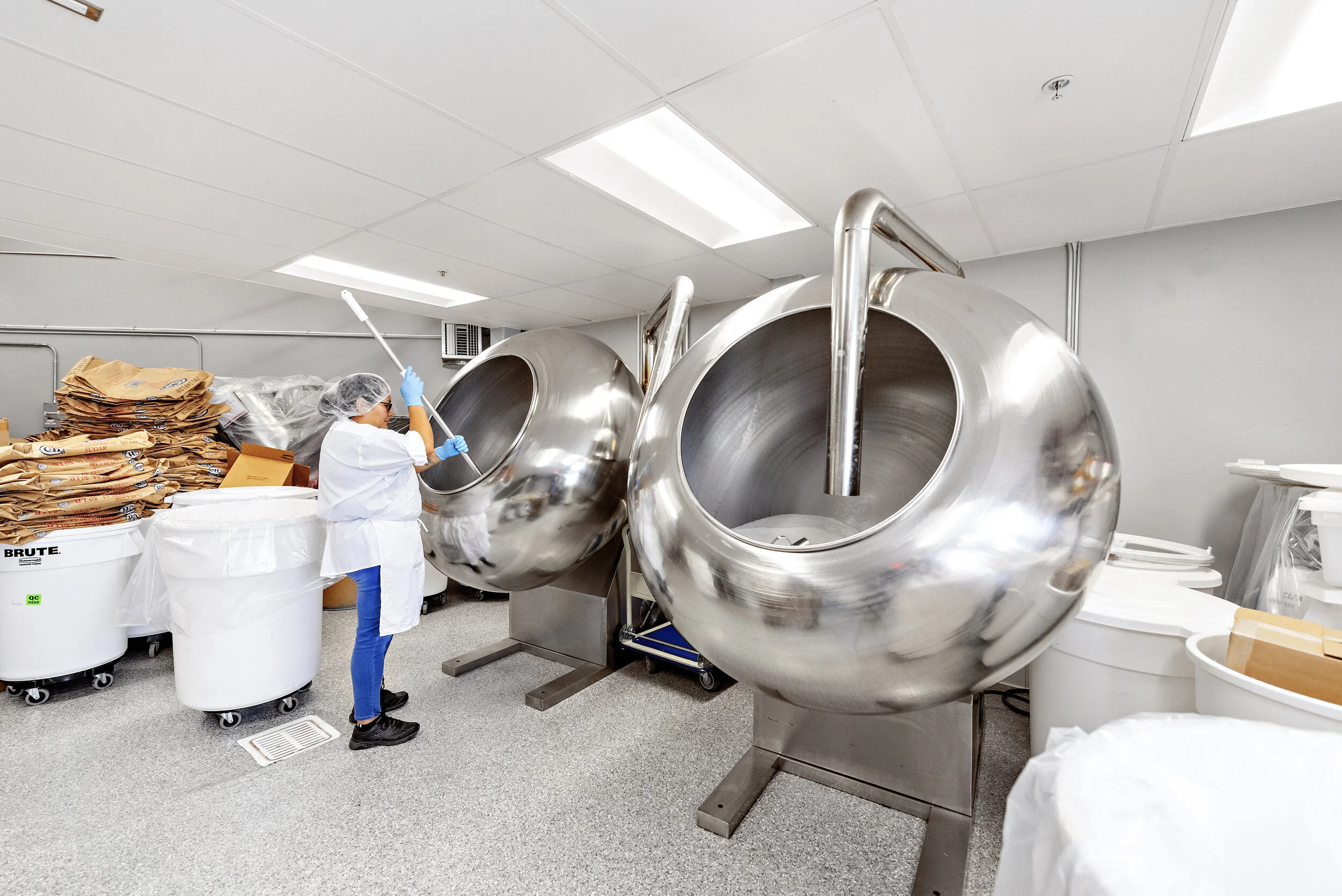 Person in protective clothing cleaning large industrial cookie mixers in a commercial bakery kitchen.