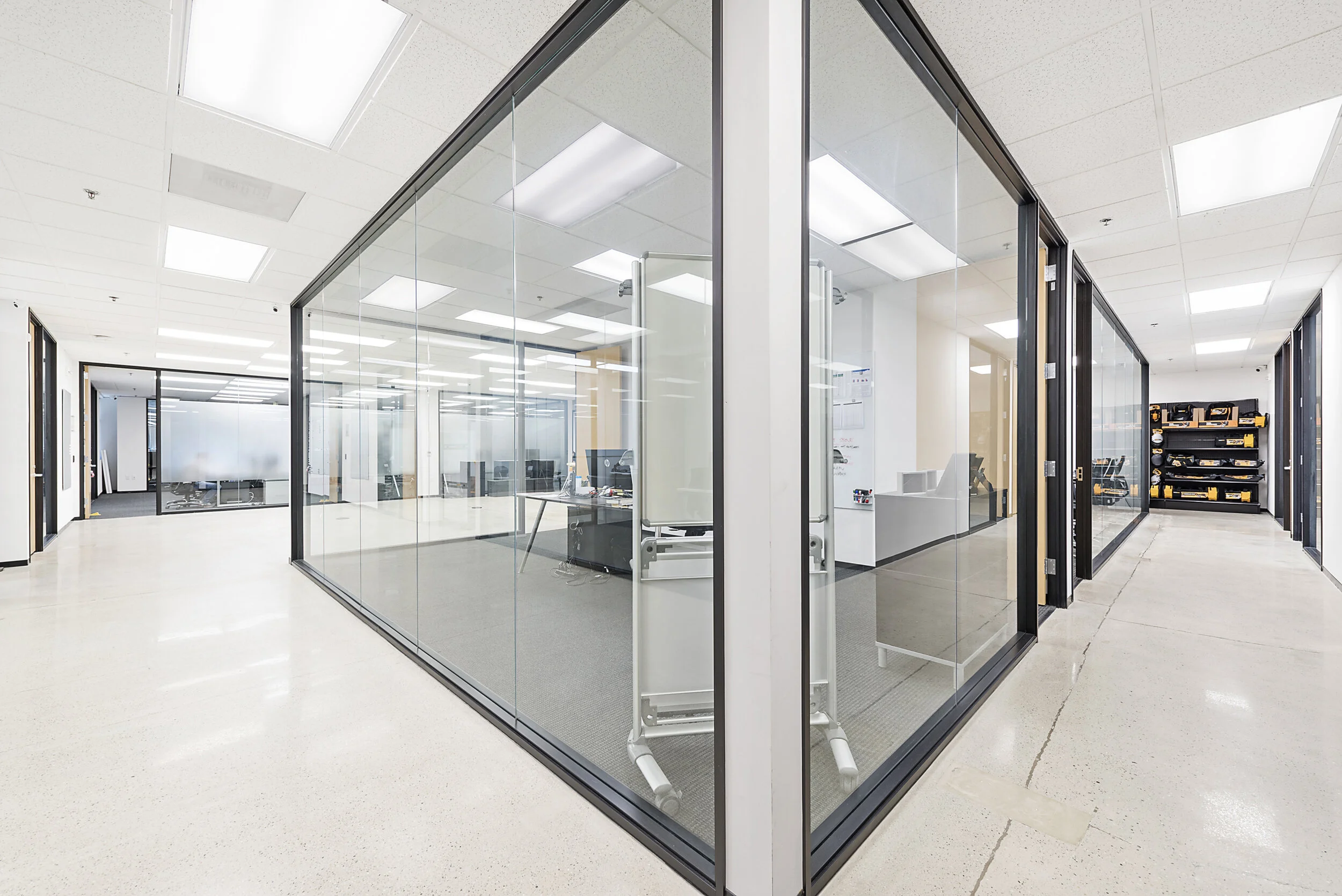 Empty office with glass-walled conference rooms and a corridor with tool storage shelves.