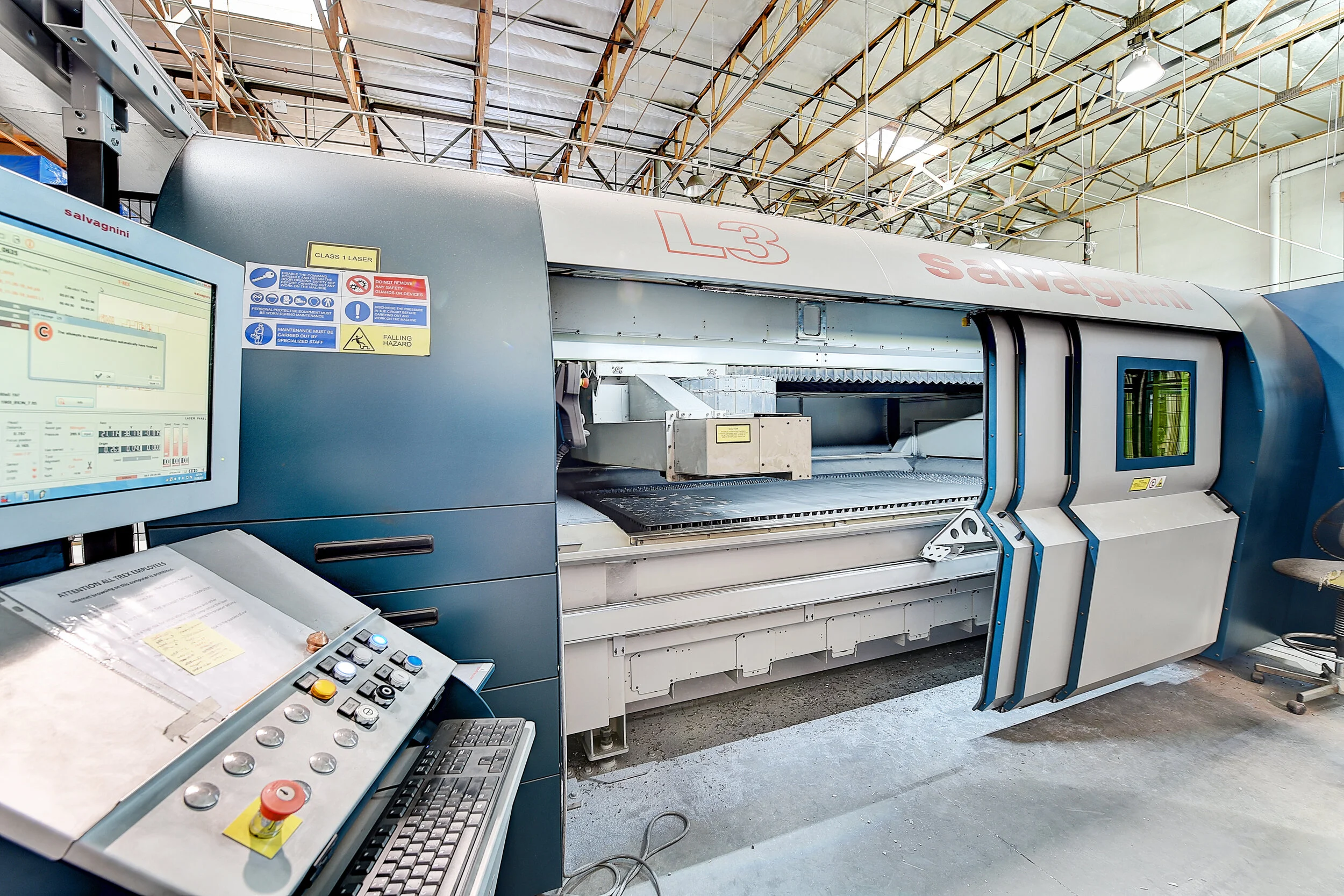 Large industrial laser cutting machine inside a factory, with control panel and computer monitor nearby.