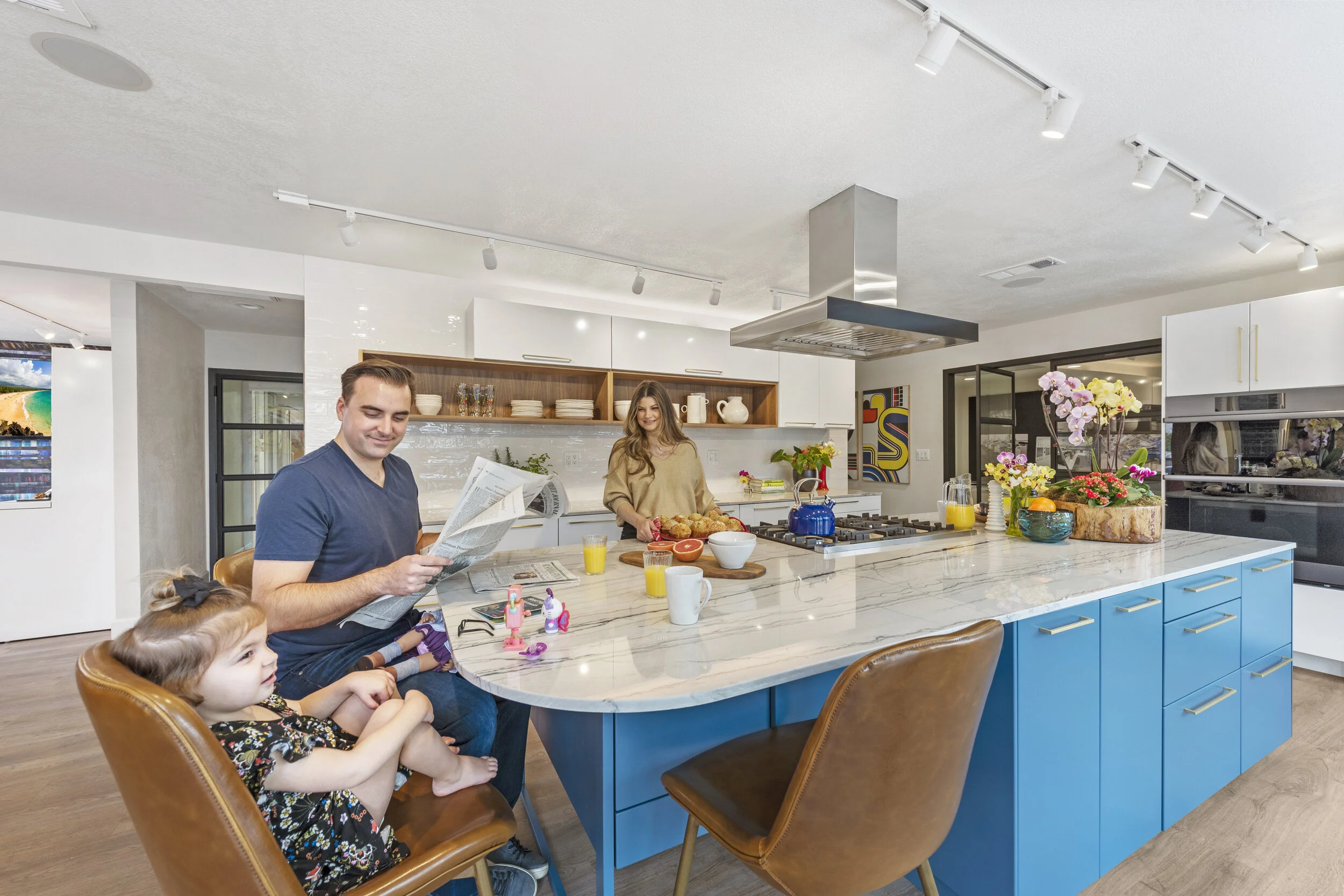 Family enjoying breakfast in a modern kitchen with blue cabinets and a marble countertop, flowers, and breakfast foods.
