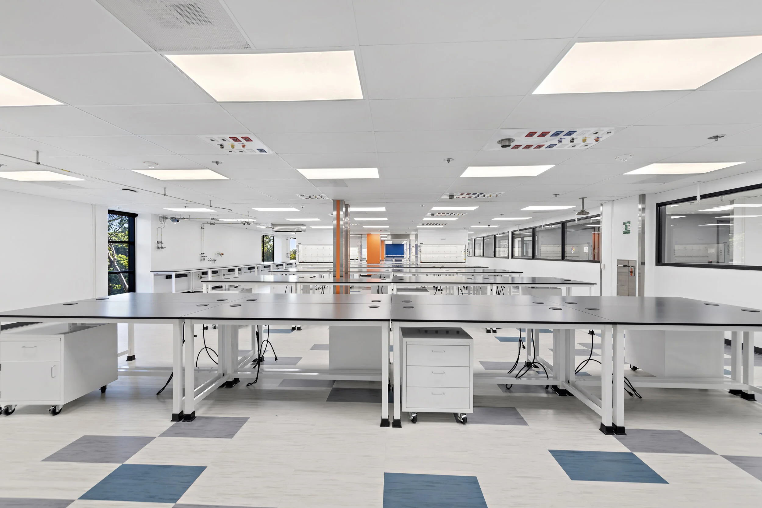 Empty modern classroom or laboratory with white walls, black tables, and large windows, well-lit with ceiling fluorescent lights.