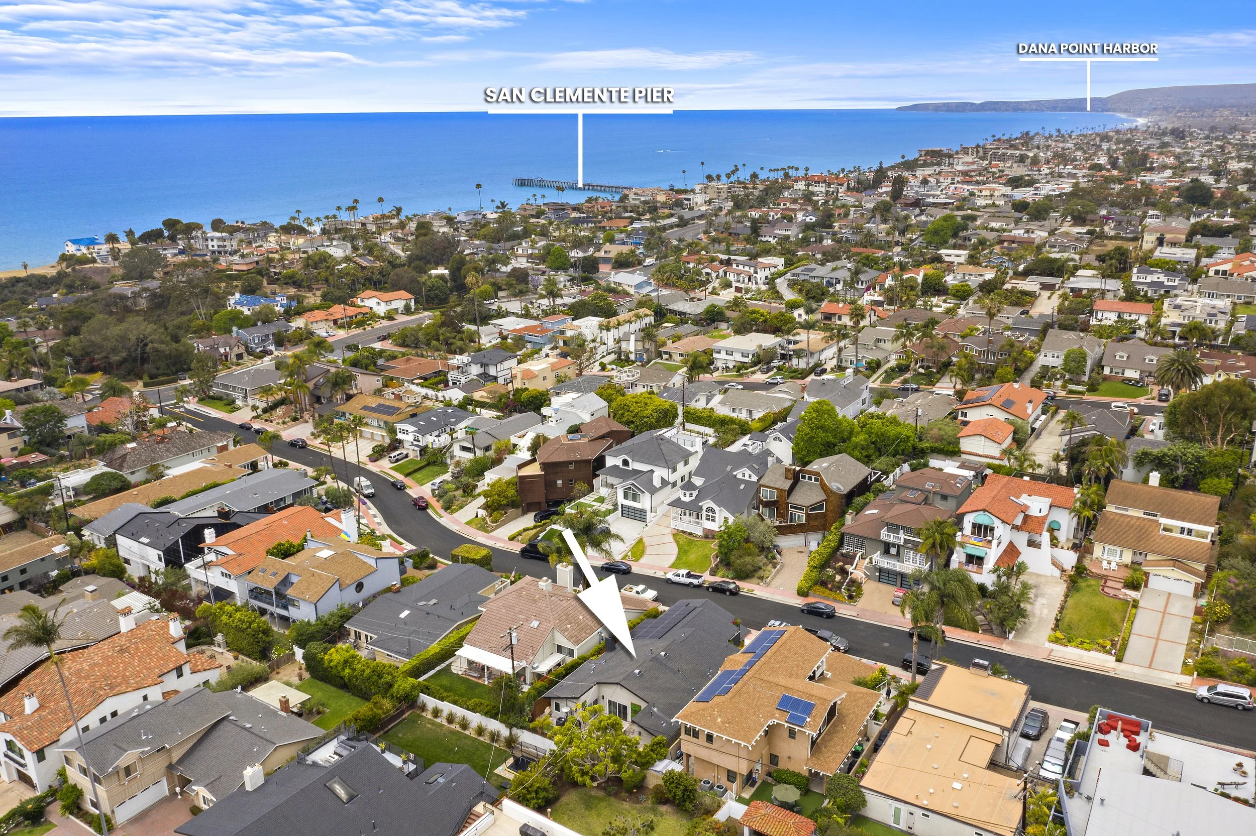Aerial view of a coastal neighborhood with houses, streets, trees, and two labeled locations, San Clemente Pier and Dana Point Harbor, with ocean in the background.