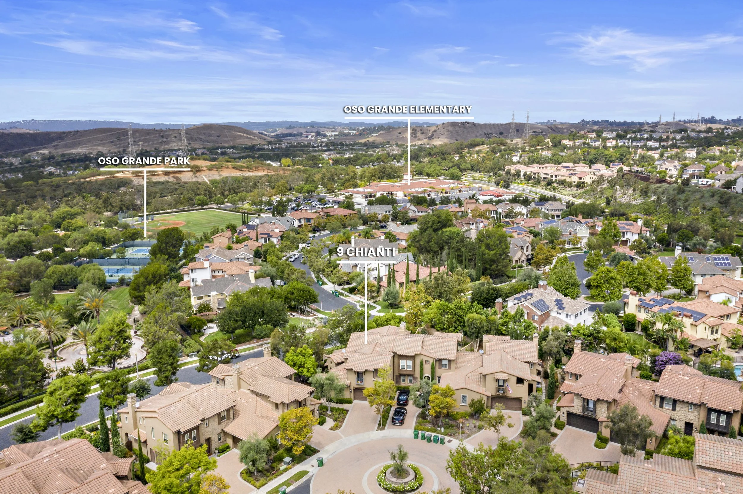 An aerial view of a residential neighborhood with labeled landmarks including Oso Grande Elementary, Oso Grande Park, and a street called 9 Chiante. The scene features houses with red-tile roofs, green trees, and mountains in the distance under a par