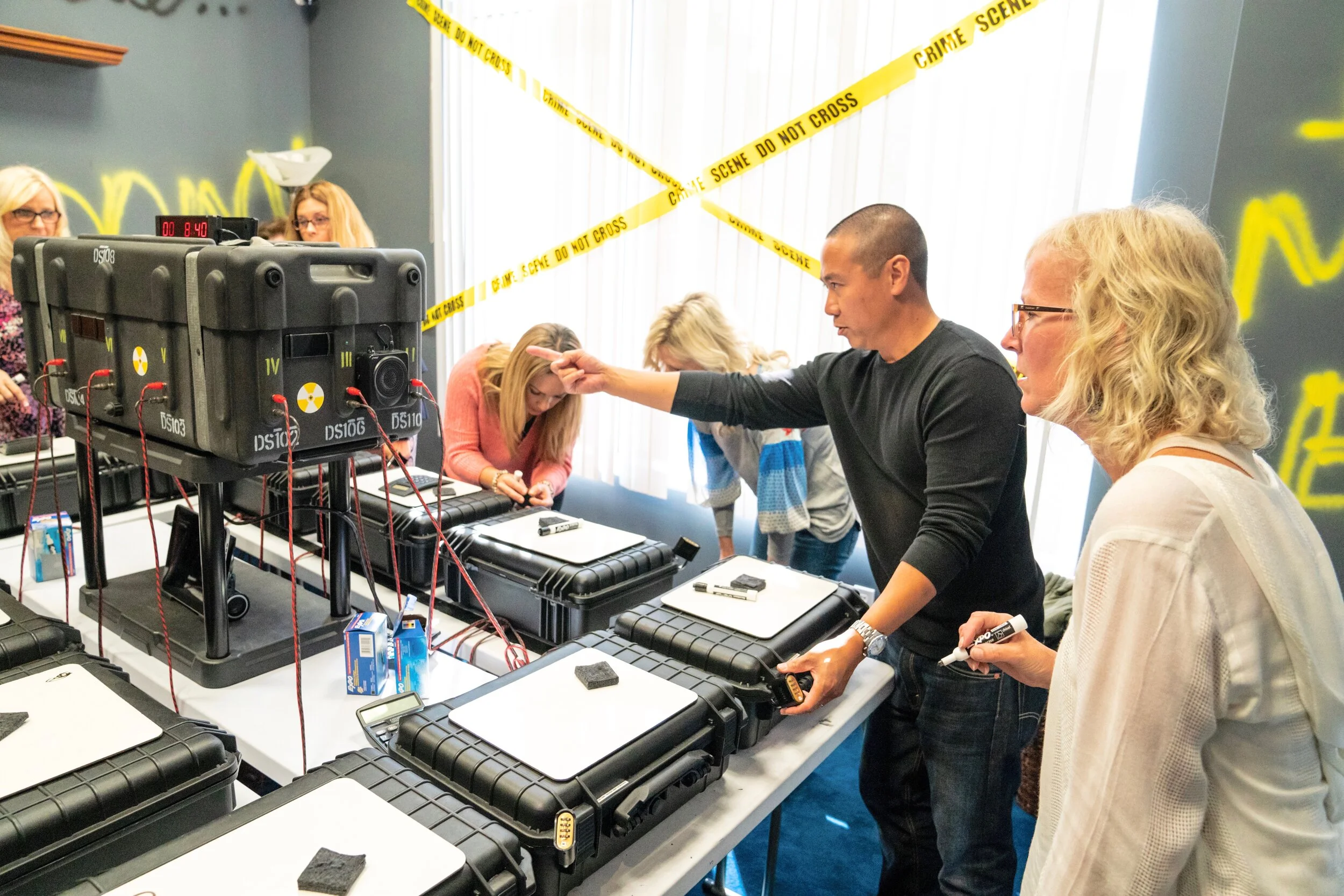 Group of people in a room with crime scene tape, working with forensic equipment and a large black case.