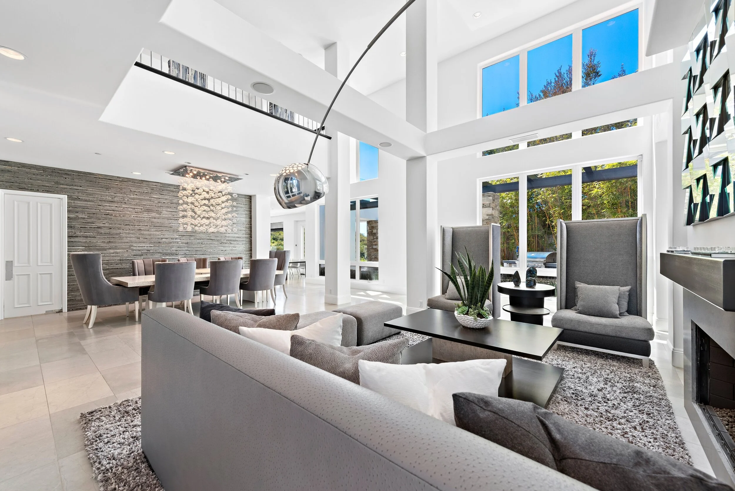 Modern open-concept living and dining room with large windows, white walls, gray seating, a dining table, and decorative accents.