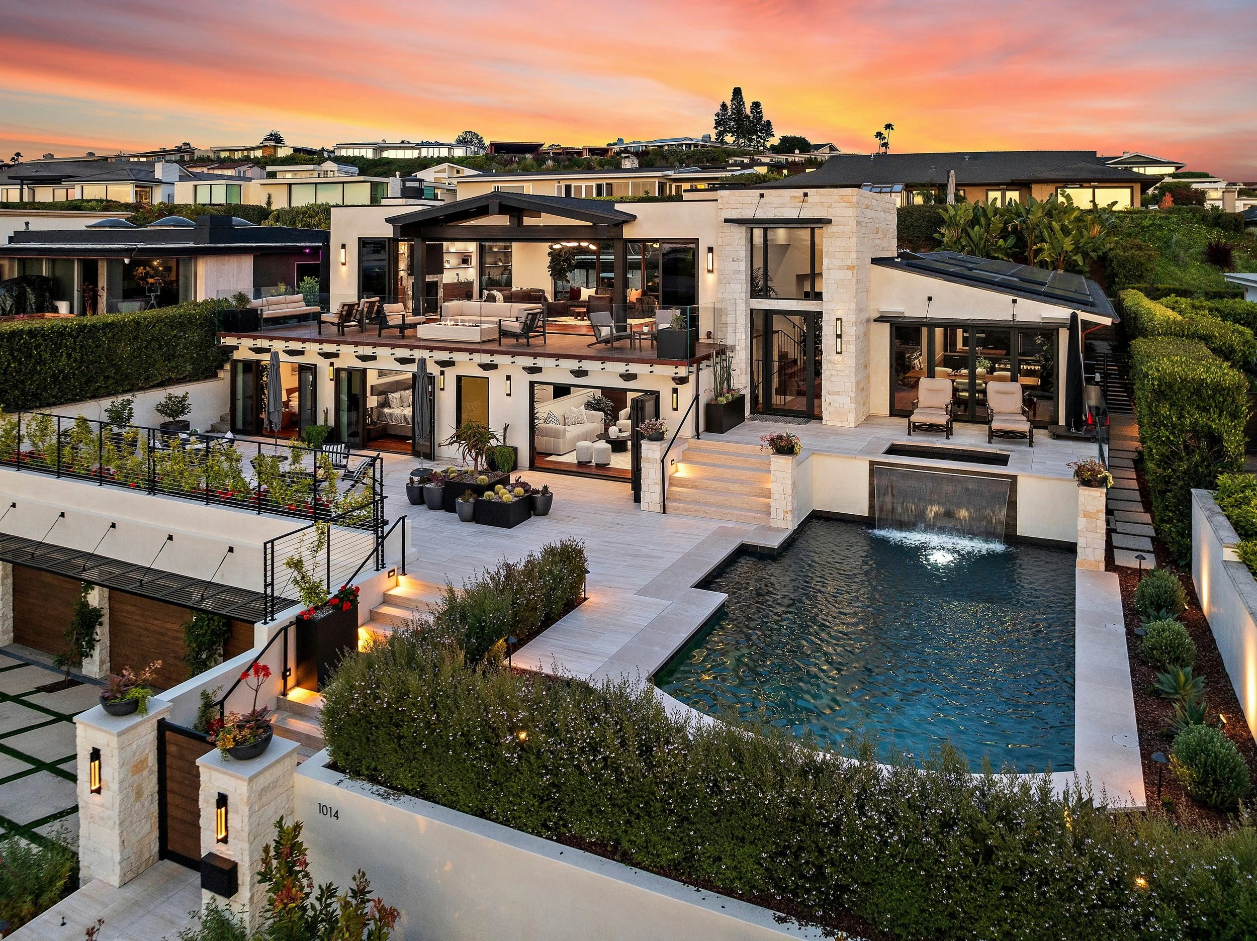 Modern multi-level house with outdoor pool, patio area, and lush landscaping during sunset.