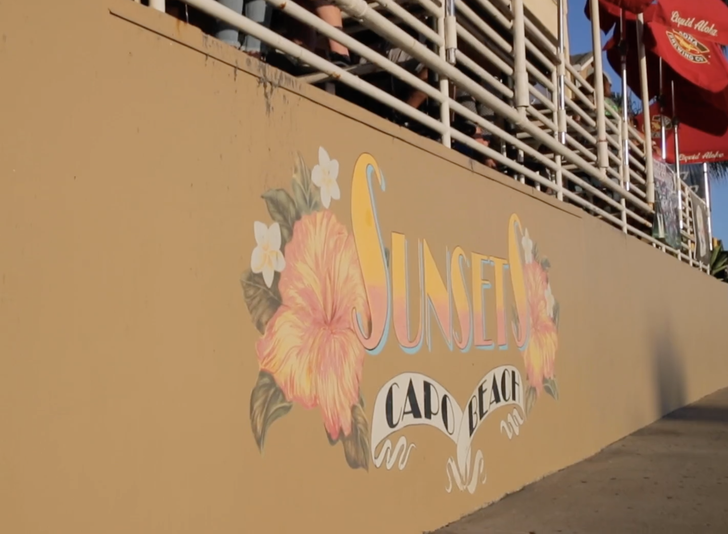 Colorful sign reading 'Sunset Cabo Beach' with tropical floral decorations on a yellow wall