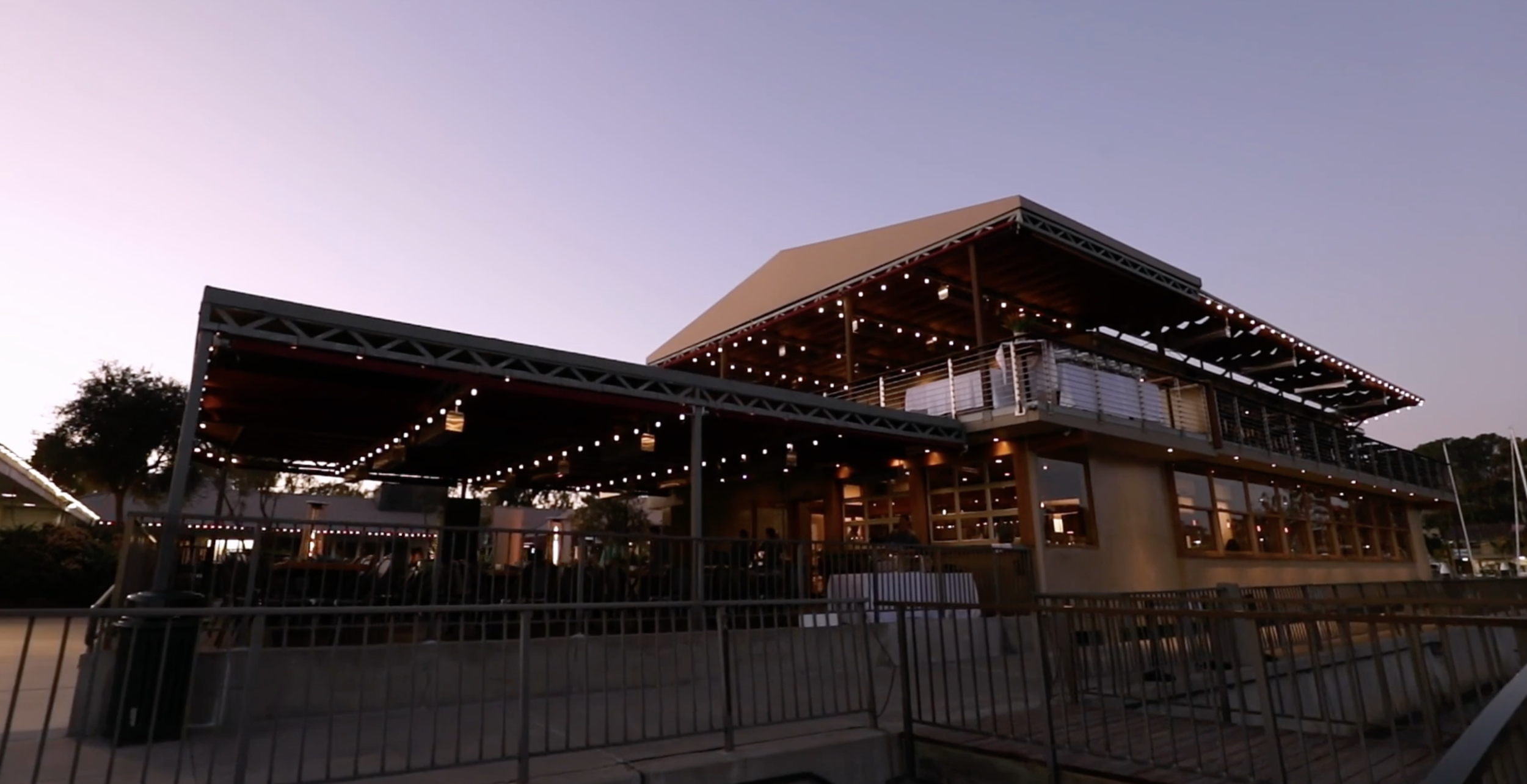 Exterior of a modern restaurant or café with string lights and large windows during sunset