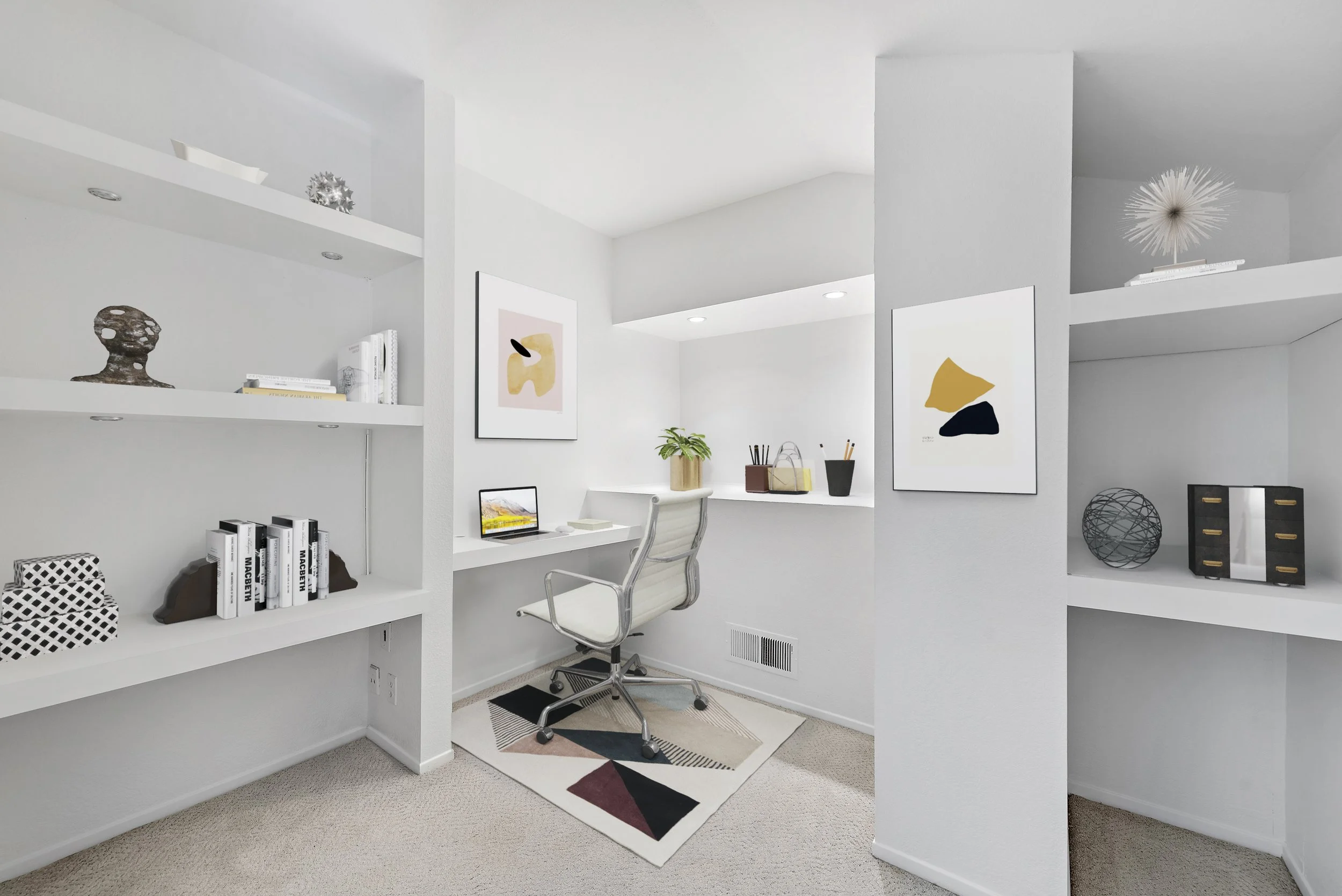 Modern white home office with built-in white shelves, abstract art, a desk with a laptop, office chair, and decorative objects.