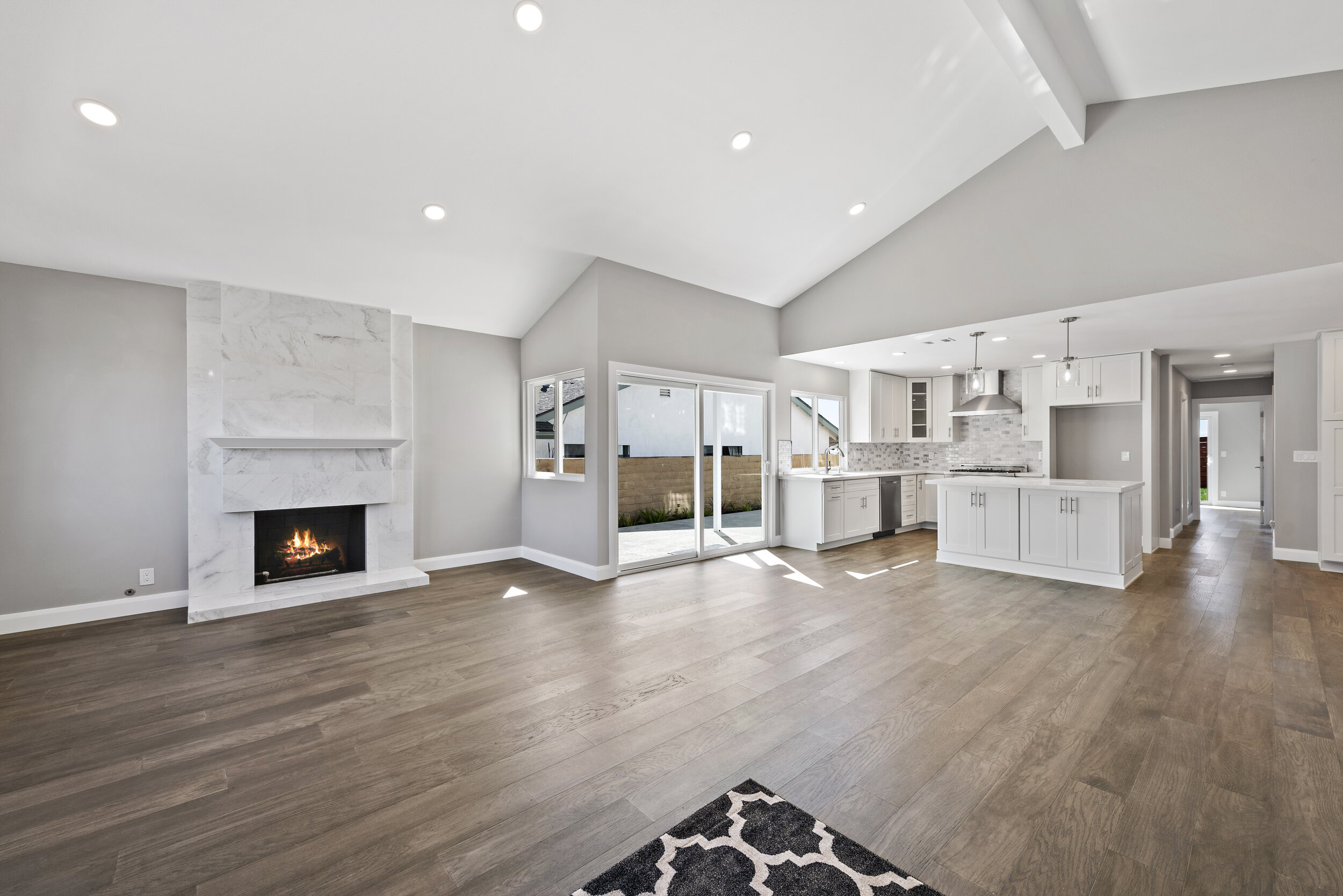 Open-concept living room and kitchen with white walls, hardwood floors, a fireplace, and sliding glass doors leading outside.