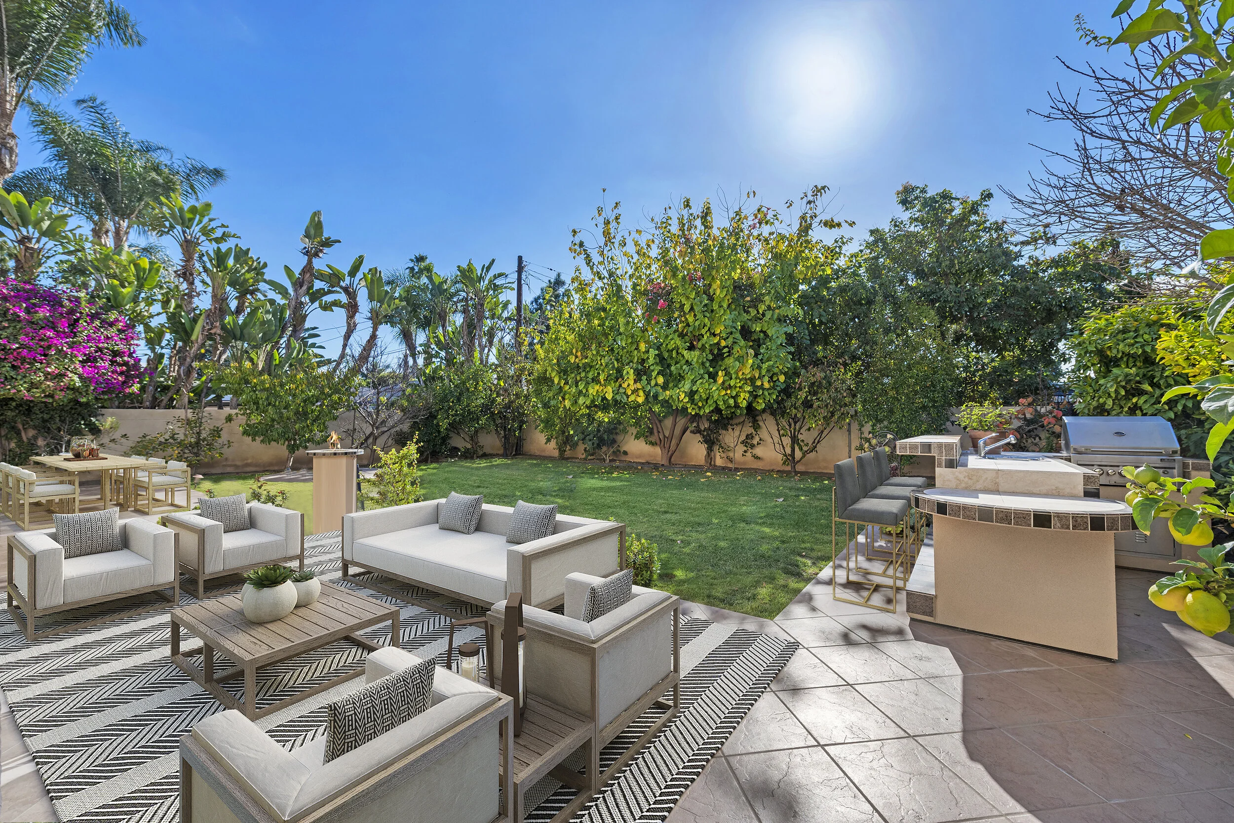 Outdoor backyard with patio furniture, BBQ grill, bar stools, lush green lawn, various trees, and a clear sunny sky.