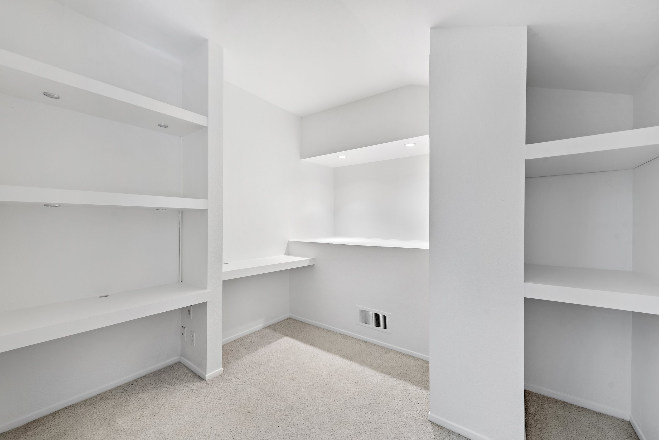 Empty white room with built-in white shelves and beige carpet.