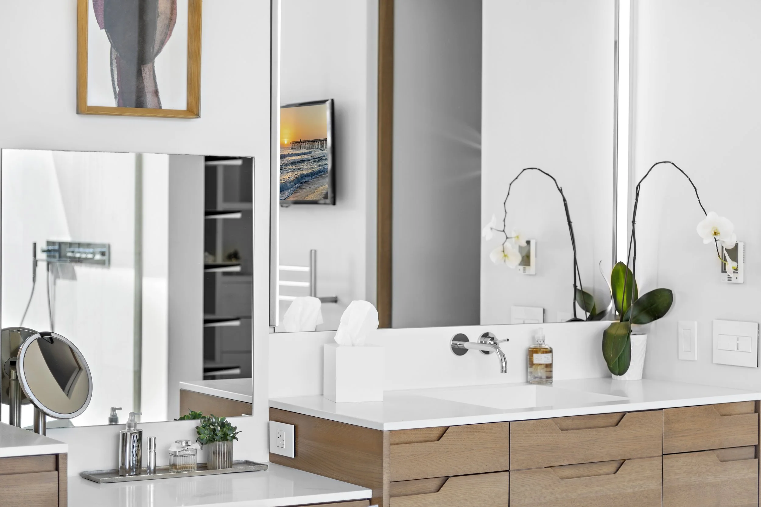 Modern bathroom vanity with a large mirror, a potted orchid, tissue box, and a soap dispenser